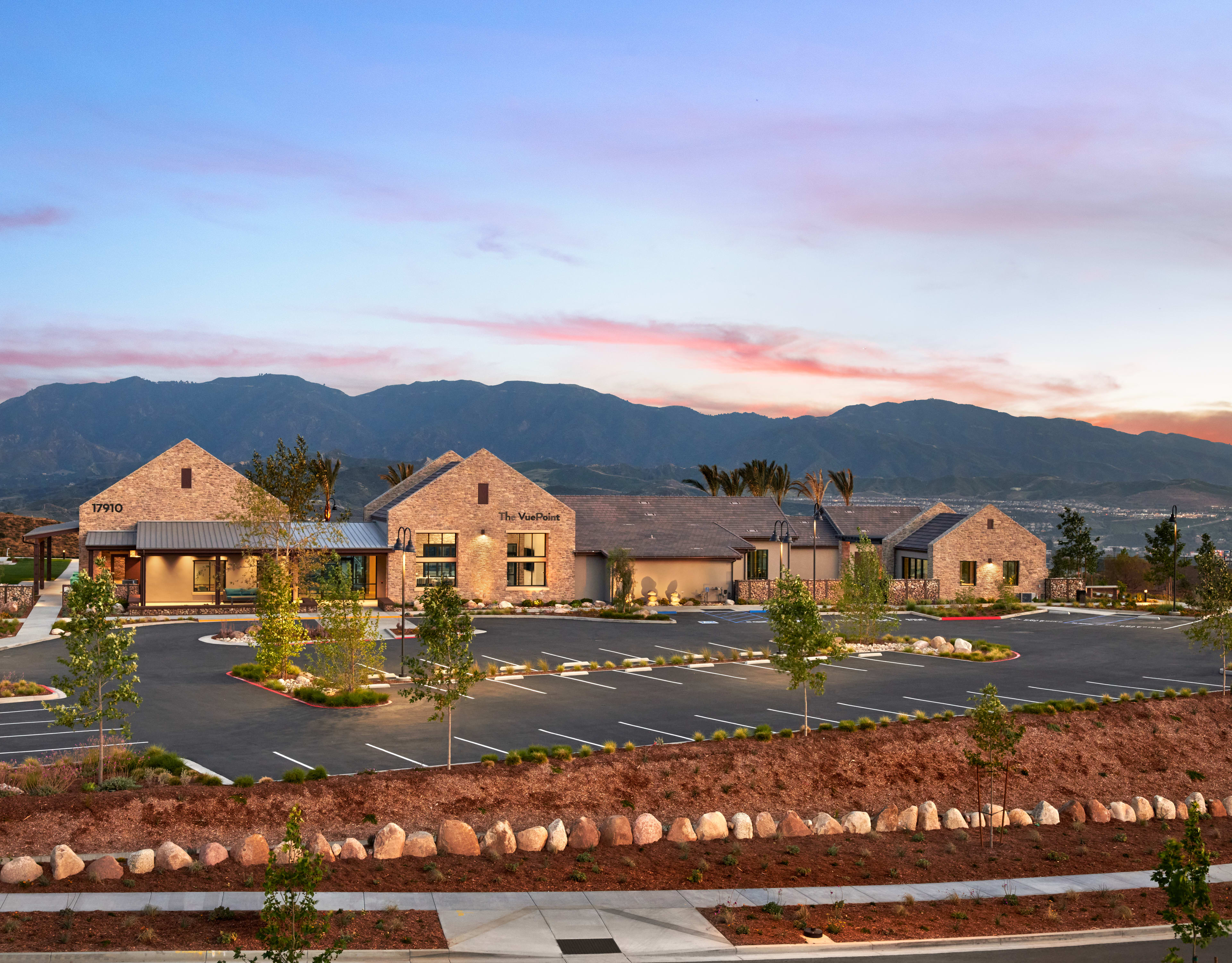 A residential community nestled against a backdrop of majestic mountains, with a well-landscaped parking lot in the foreground.