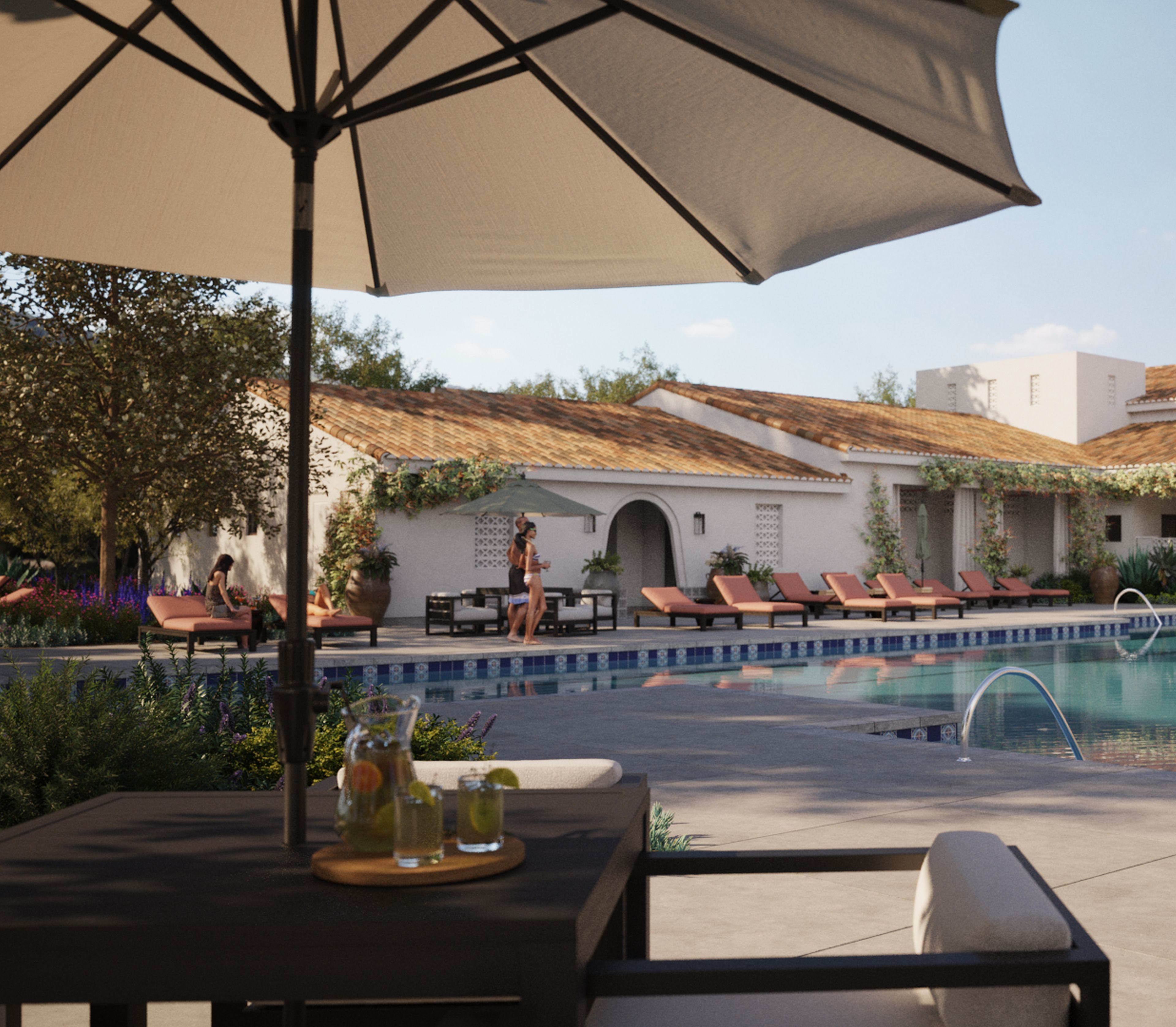 A serene outdoor pool area surrounded by white buildings with red tile roofs, shaded by a large umbrella and featuring lounge chairs and tables with drinks.