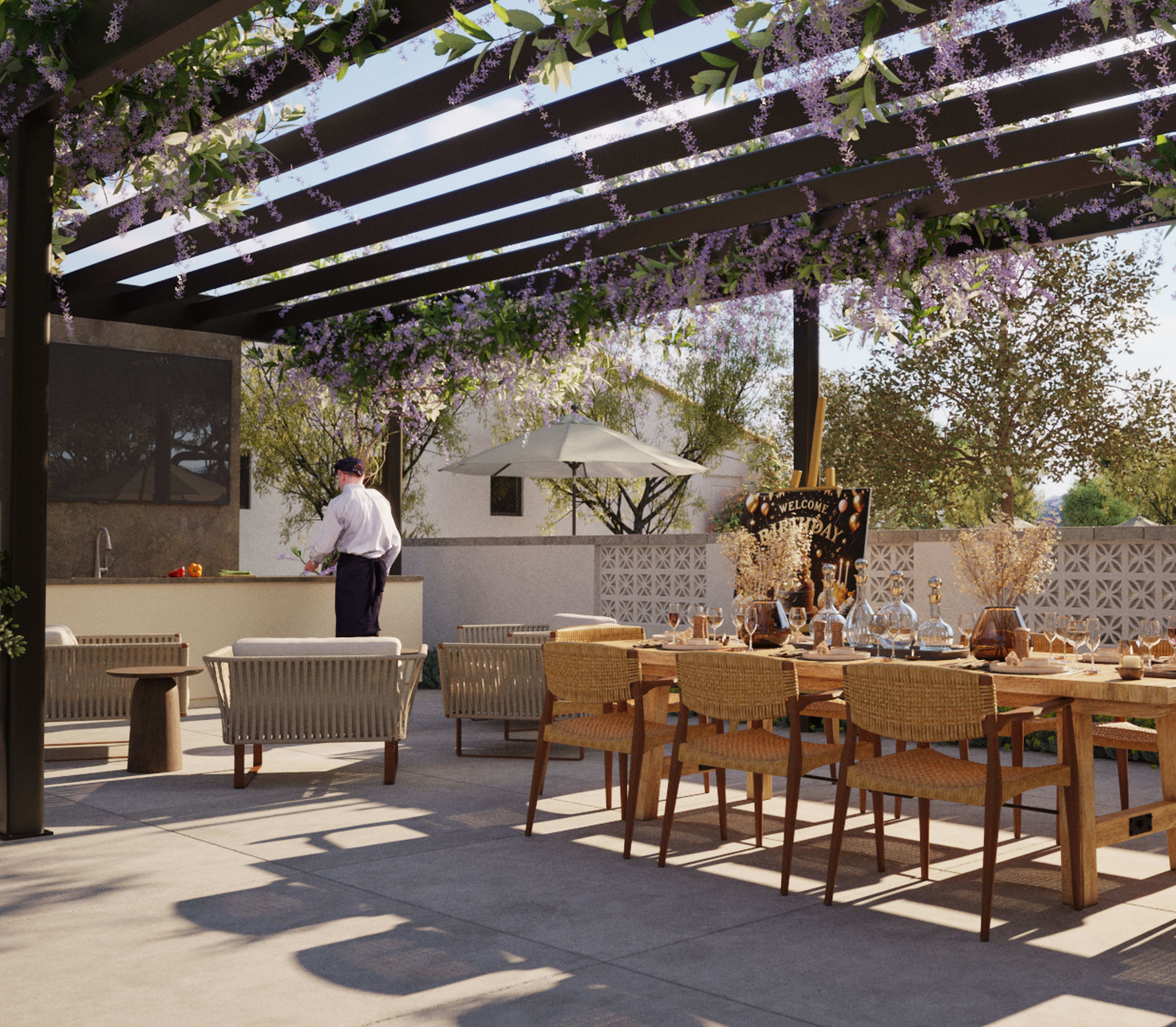 An outdoor dining area with a wooden pergola overhead, surrounded by lush greenery and potted plants, with a table and chairs set up for an alfresco meal.