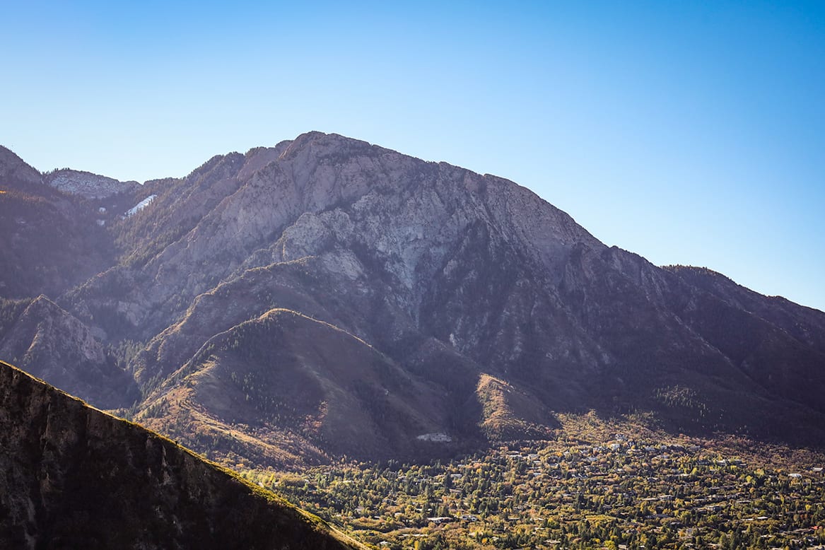 Rugged, snow-capped mountains rise majestically against a clear blue sky, overlooking a lush, verdant valley below.