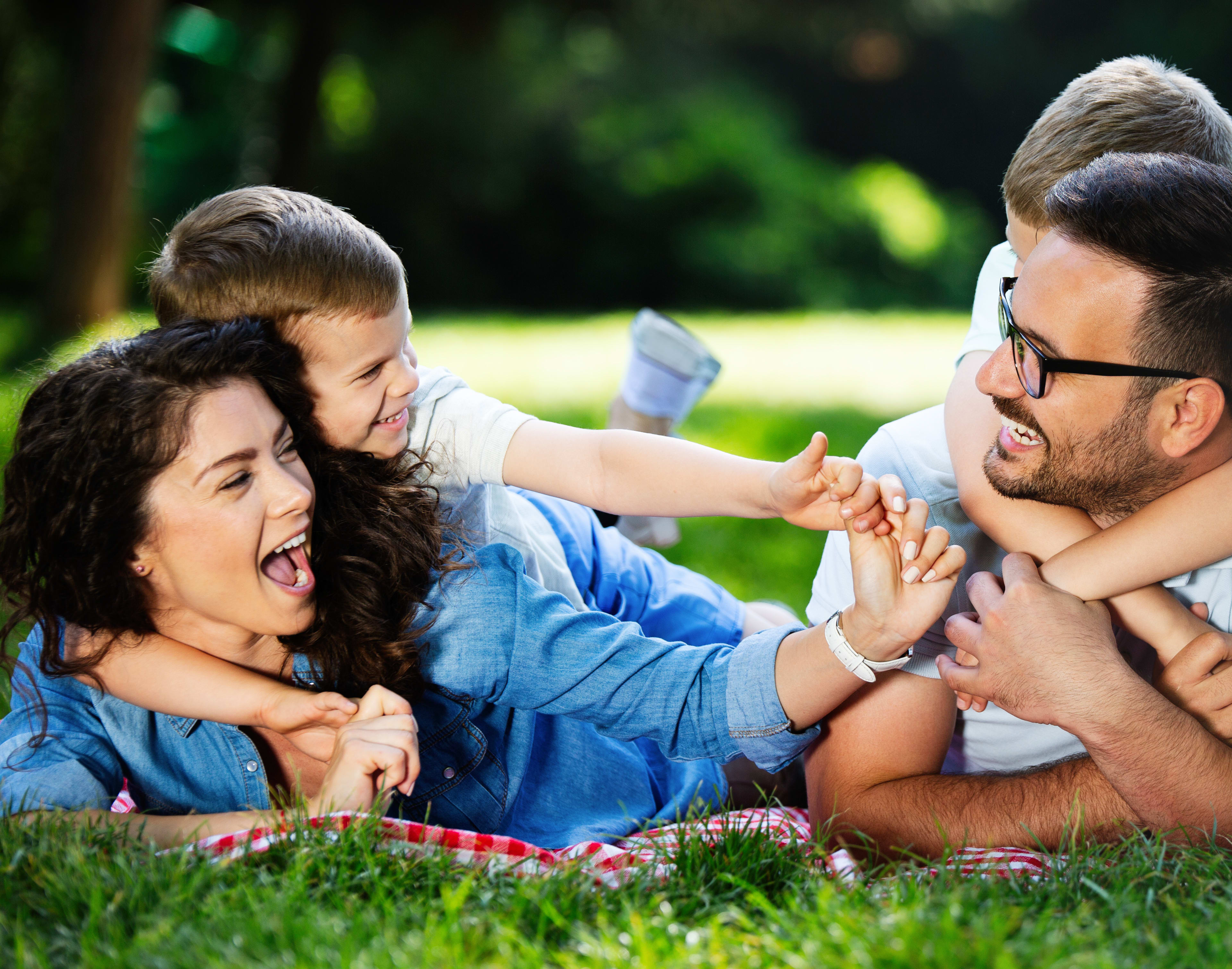 A happy family enjoying a picnic in a lush, green outdoor setting, with the adults playfully interacting with the child.
