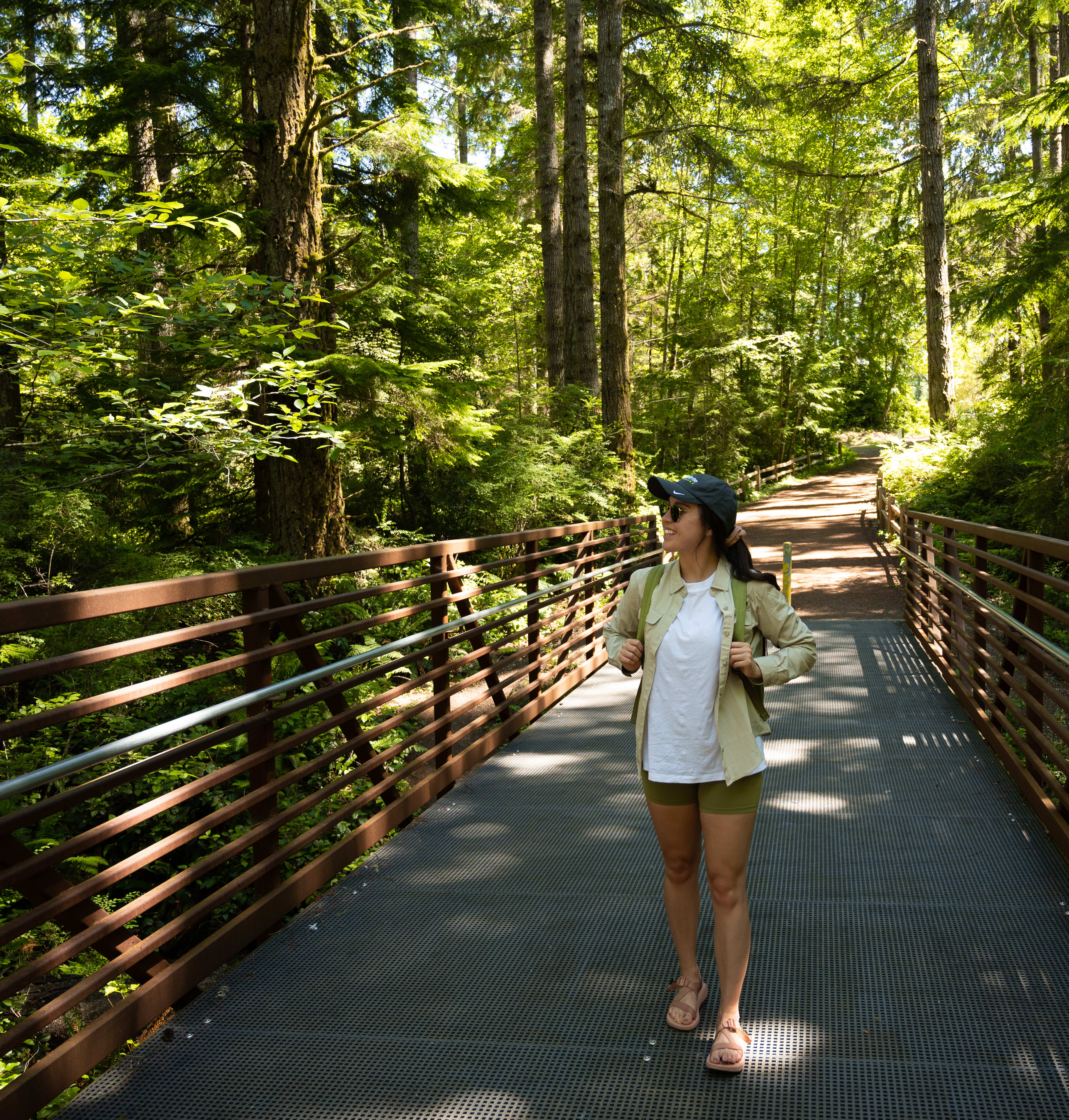 A woman in a white dress walks along a wooden bridge surrounded by a lush, green forest.