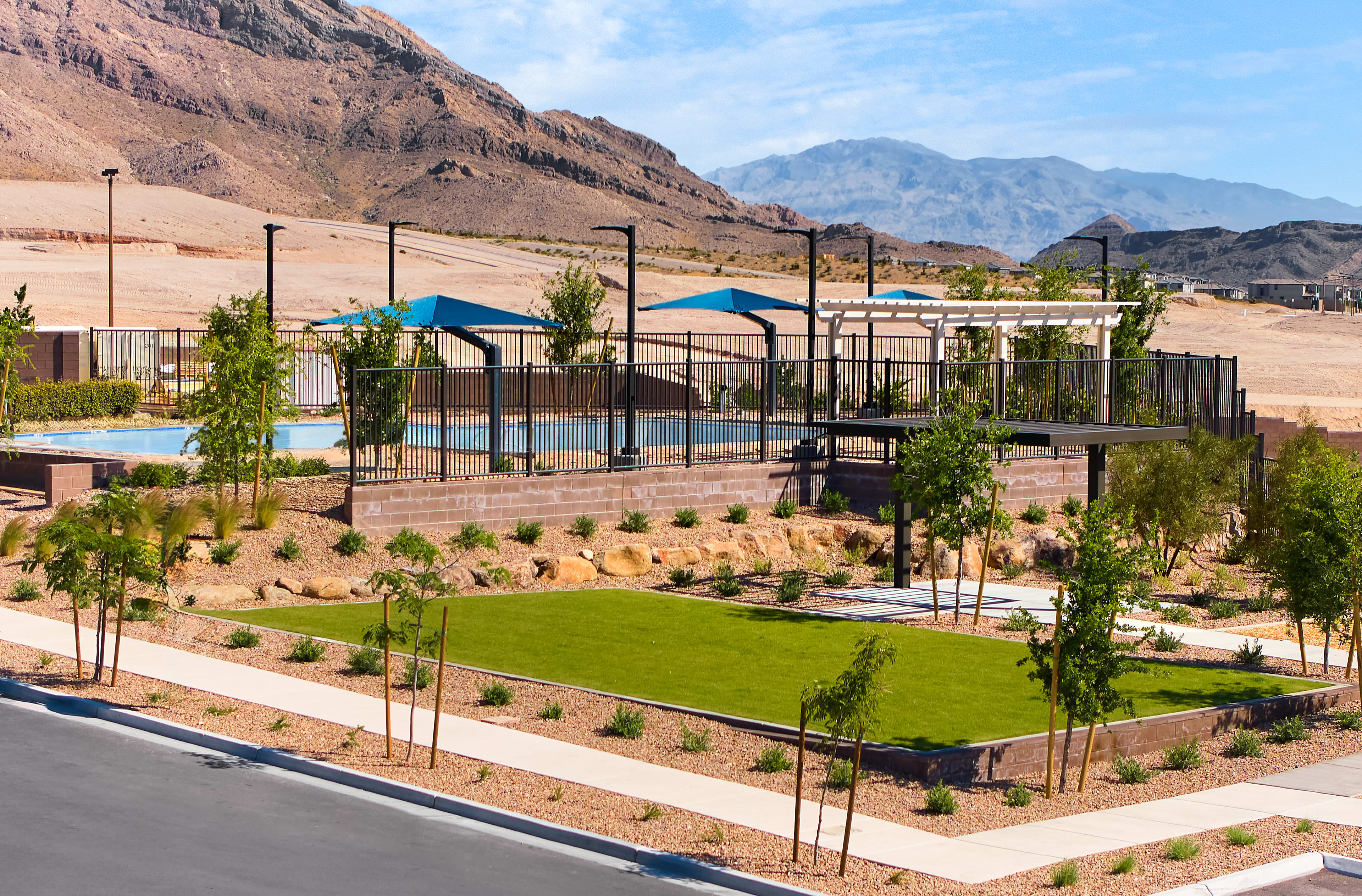 A well-designed outdoor recreational area with a lush green lawn, shaded seating areas, and a basketball court, set against the backdrop of rugged, mountainous terrain.