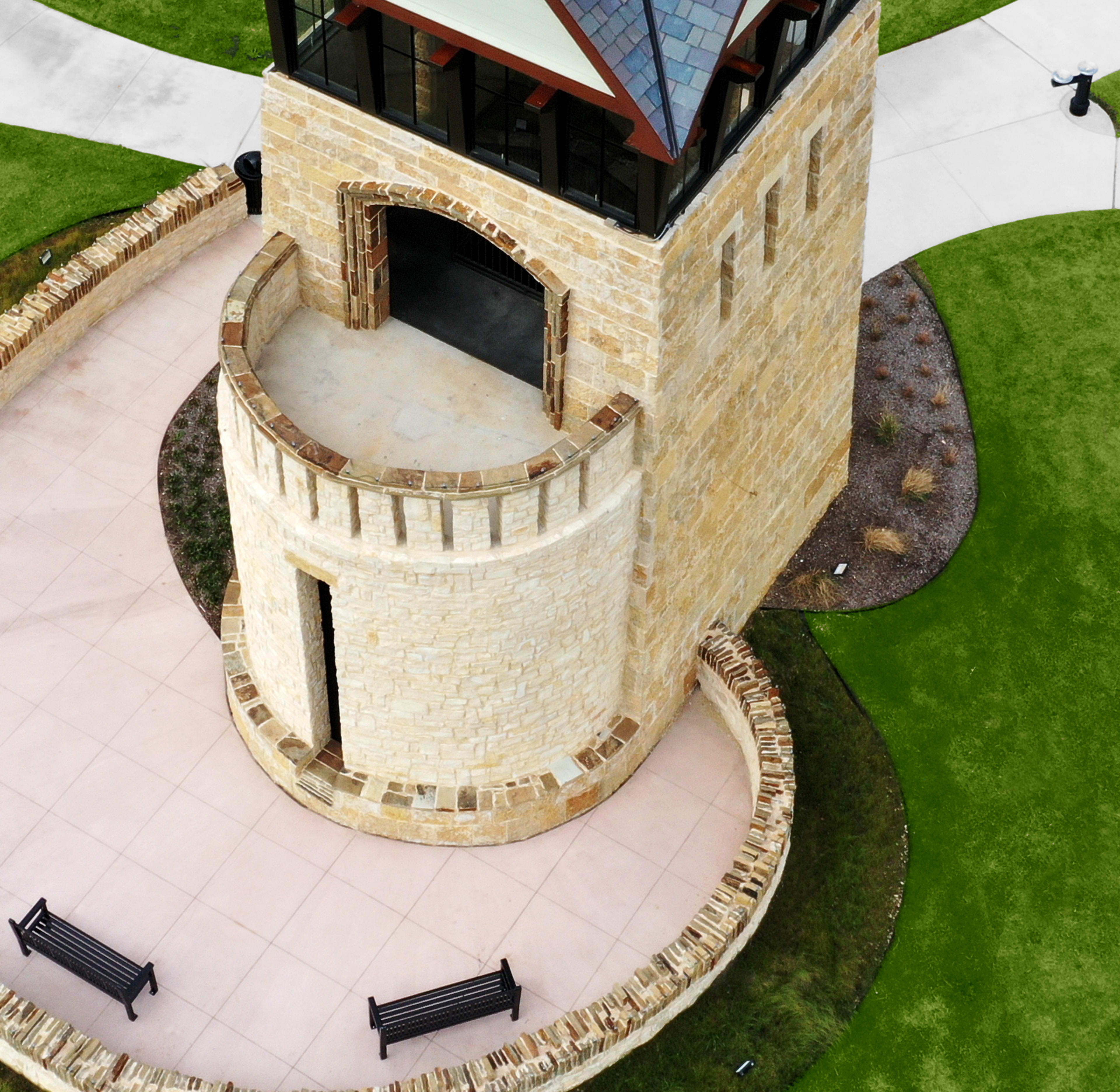 A stone tower stands on a grassy mound, surrounded by a circular path with benches, against a backdrop of lush green hills.