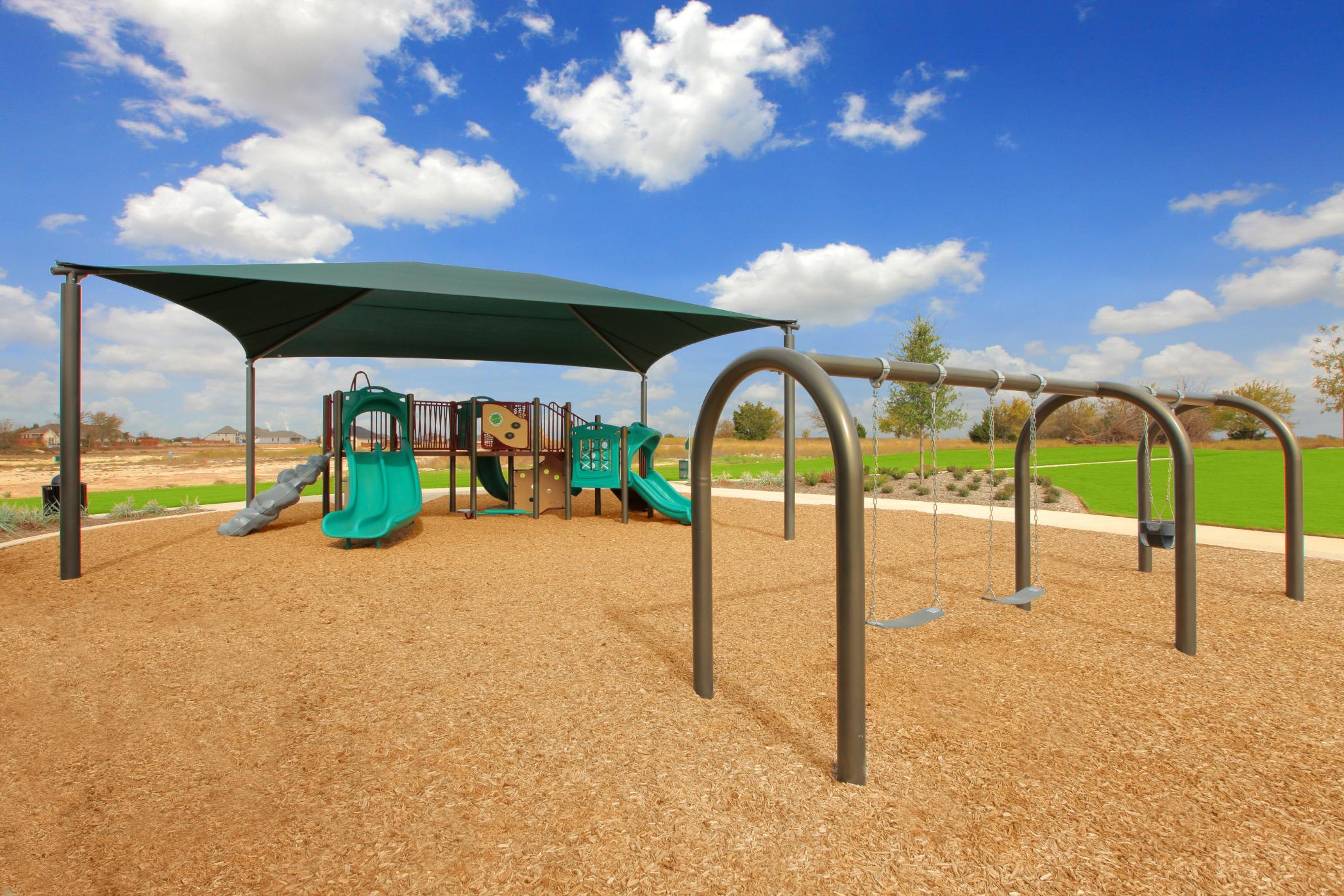 A playground with various colorful play equipment, including slides and climbing structures, set against a backdrop of a blue sky with fluffy white clouds.
