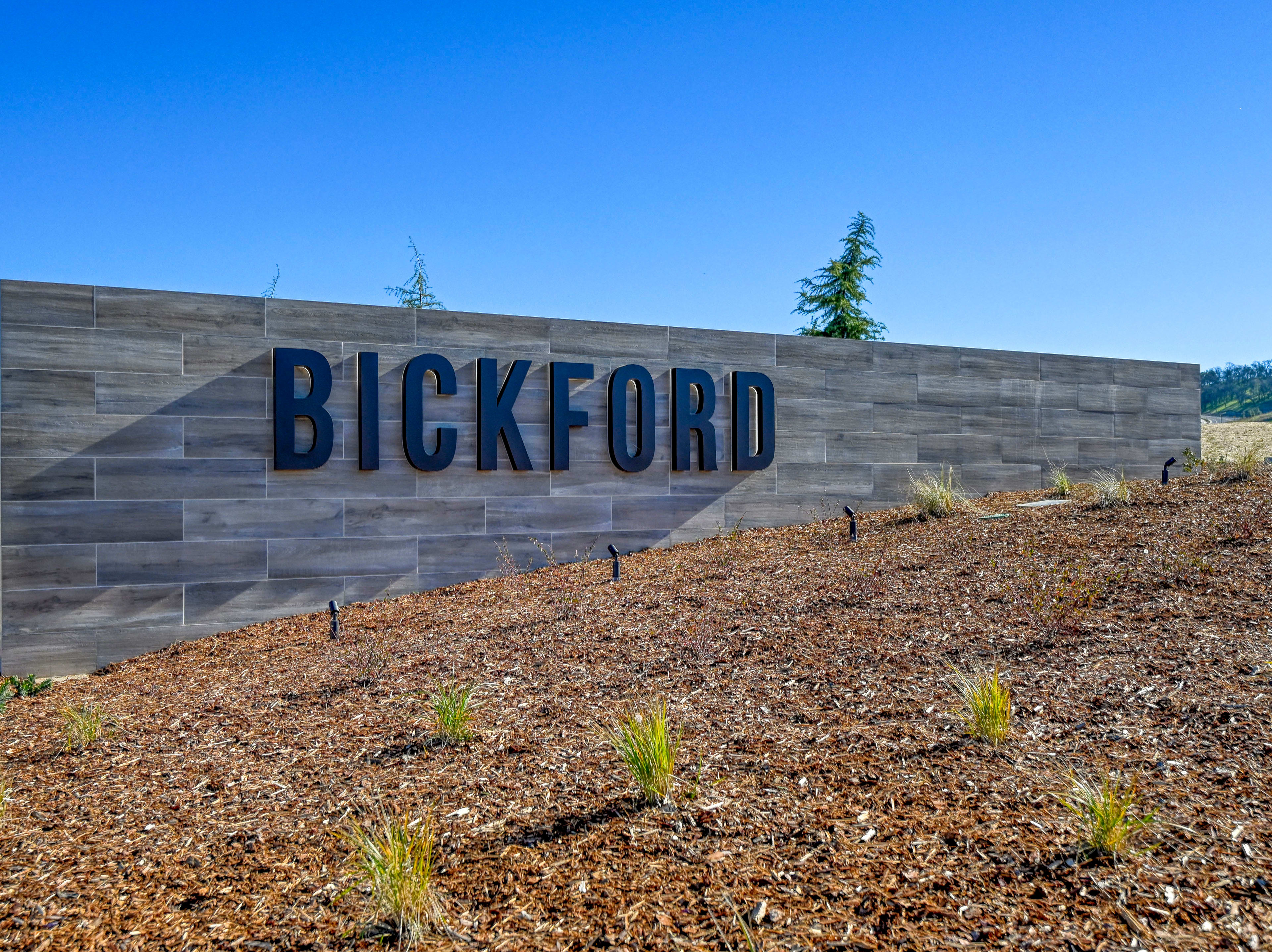 A large sign displaying the name "BICKFORD" stands prominently against a clear blue sky, with a grassy slope and a few trees visible in the foreground.