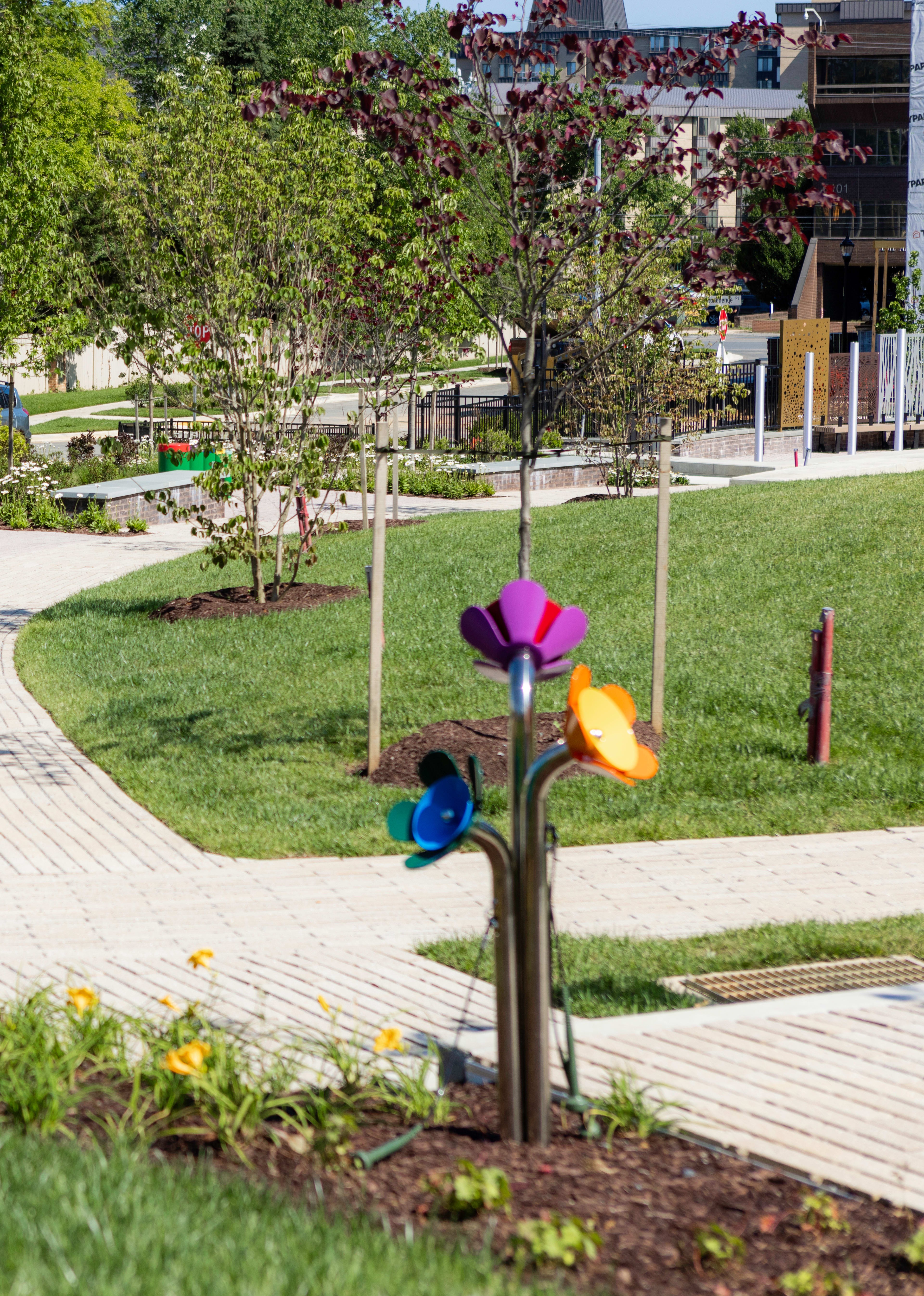 A well-maintained garden path winds through a lush, green landscape, with colorful sculptures and decorative elements lining the walkway, creating a vibrant and inviting outdoor space.