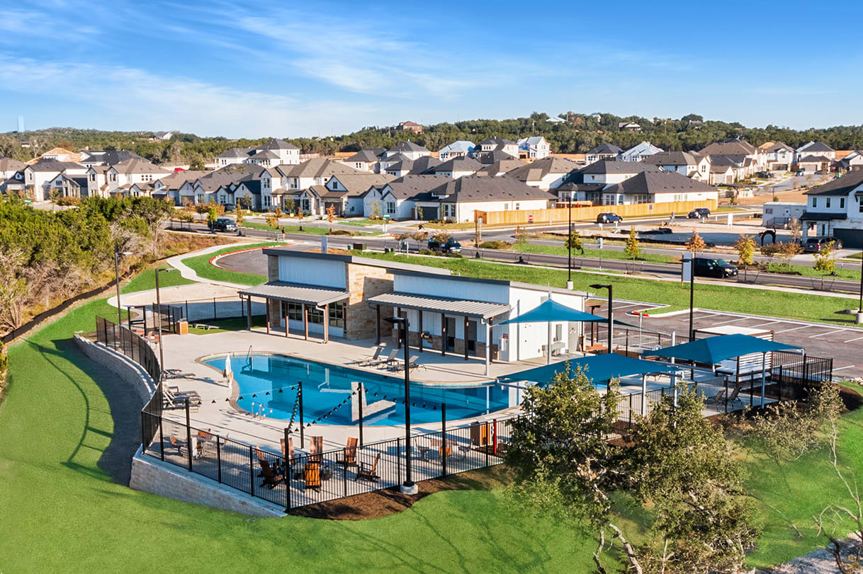 A residential neighborhood with a community pool and recreational facilities surrounded by rolling hills and a clear blue sky.
