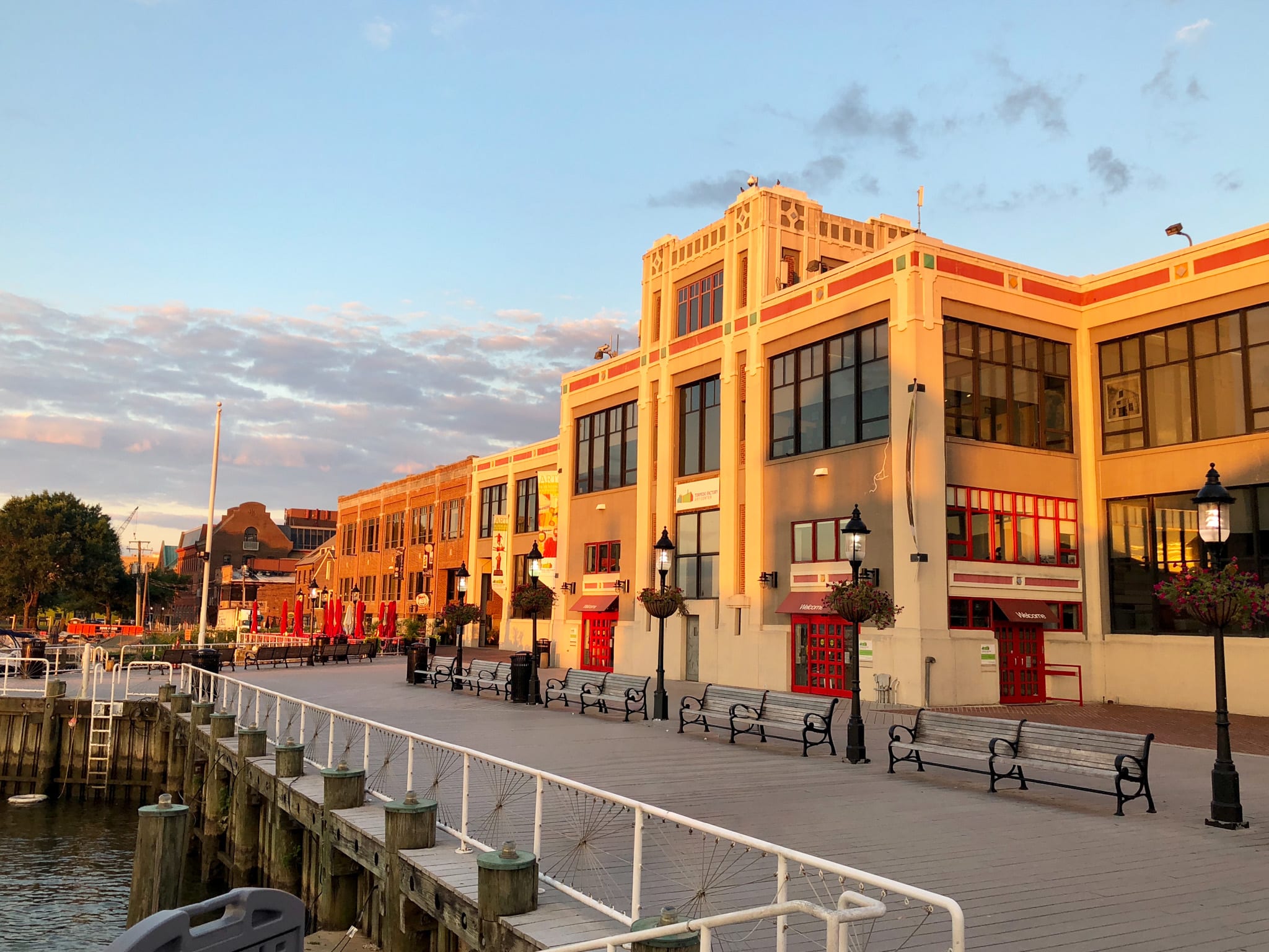 A waterfront promenade lined with colorful, ornate buildings against a backdrop of a cloudy sky at sunset.