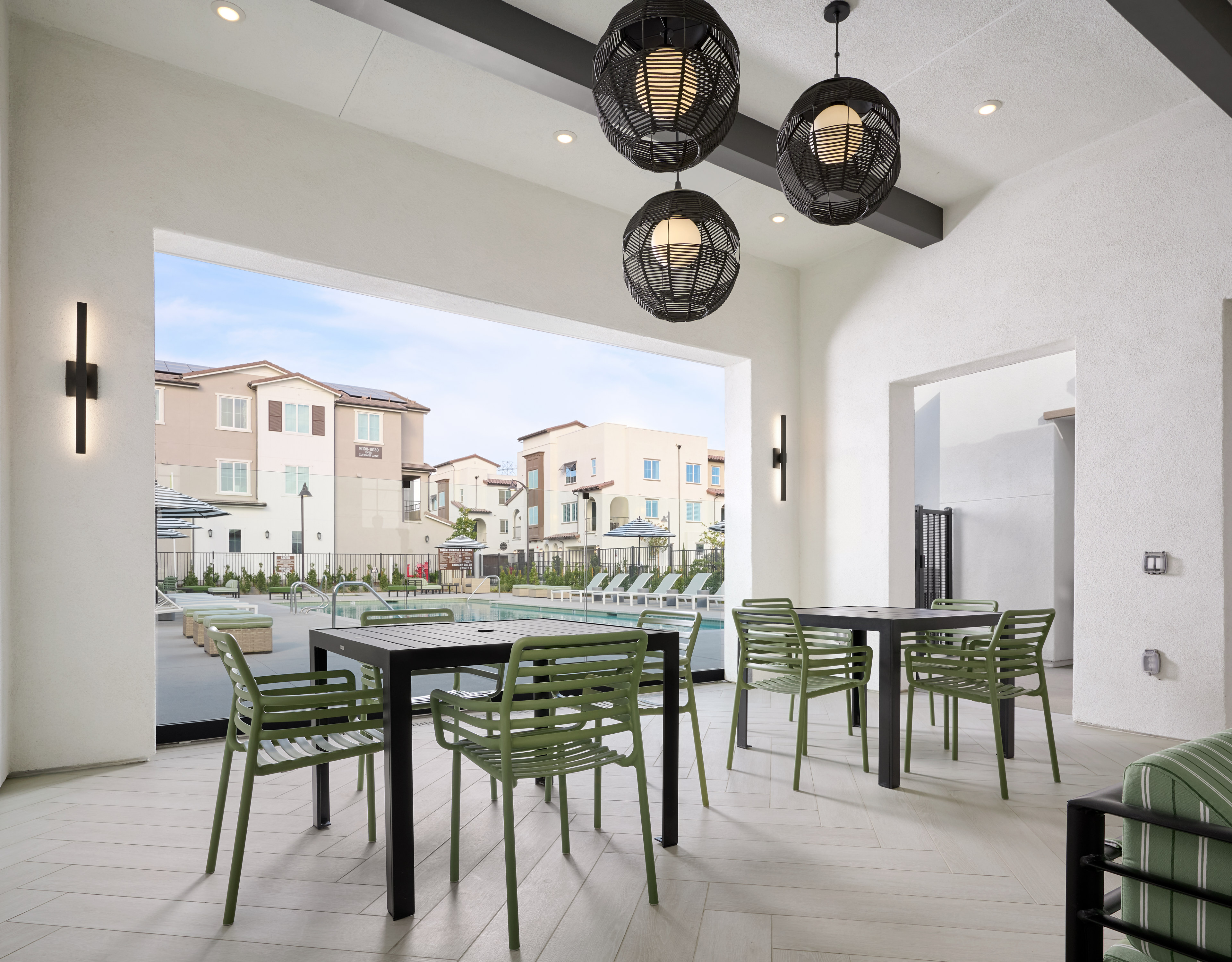 A modern and spacious dining area with a table and chairs, surrounded by a scenic outdoor view of a residential neighborhood through a large window.