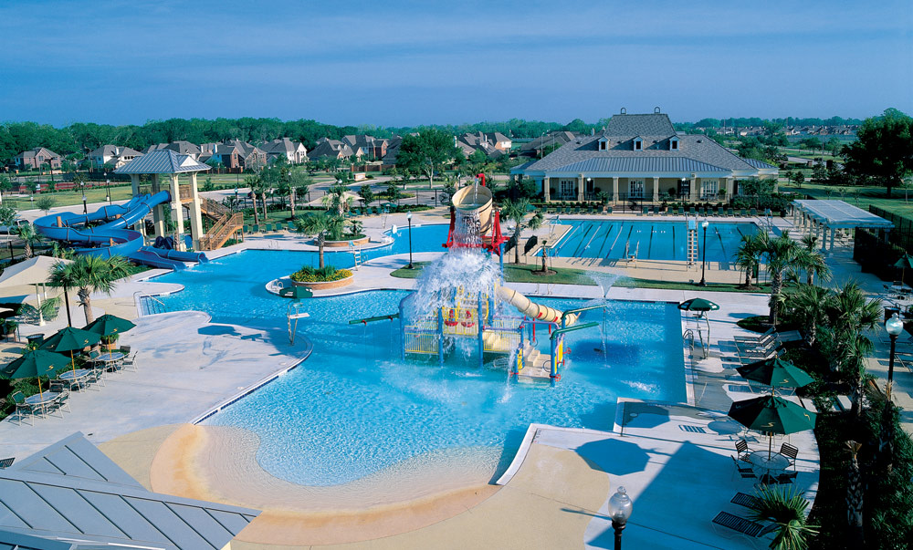 A large, colorful water park with multiple pools, slides, and other attractions surrounded by lush greenery and buildings in the background.