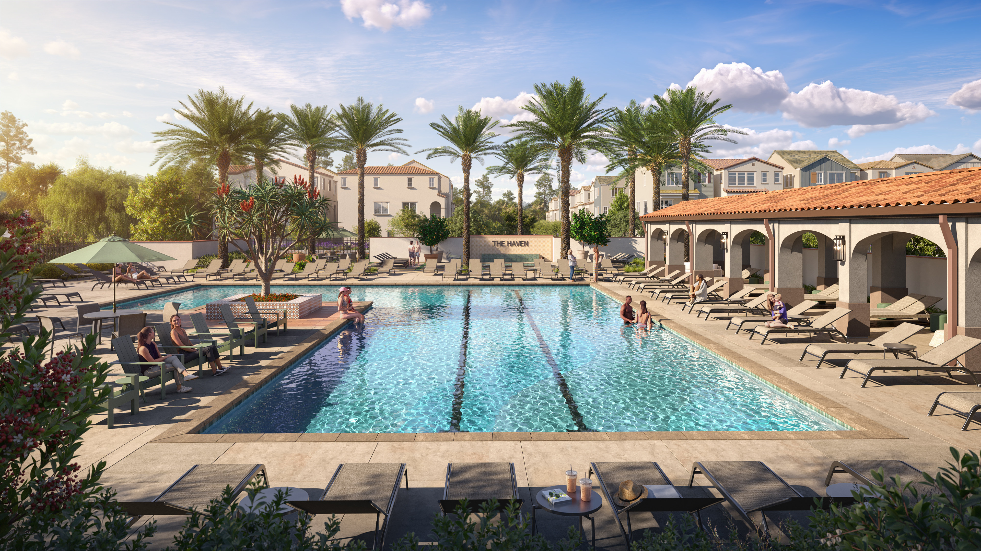 People relax on lounge chairs around a large swimming pool with palm trees and houses in the background.