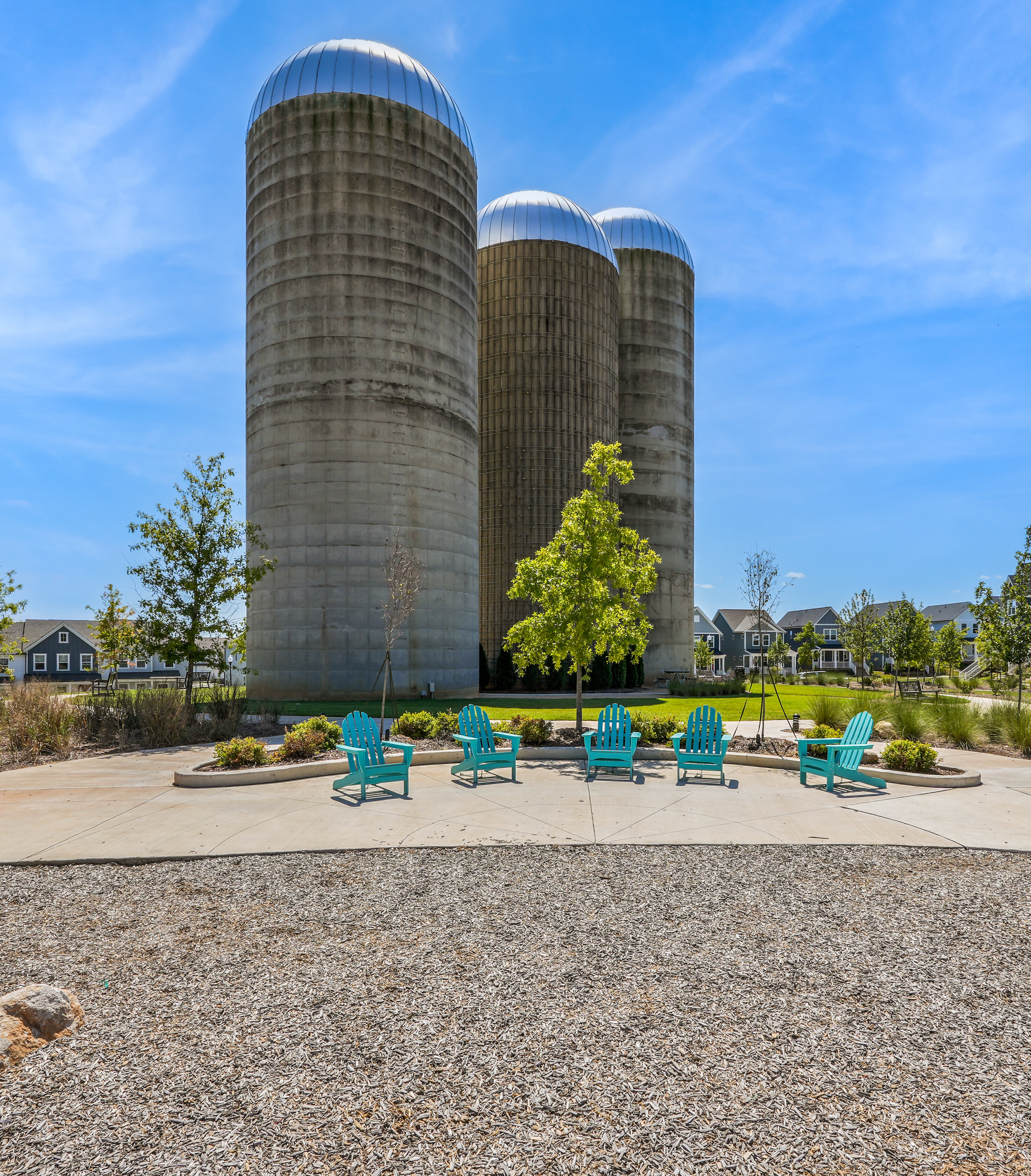 The image depicts a scenic outdoor area with three large silos in the background, surrounded by a grassy landscape with colorful Adirondack chairs in the foreground.