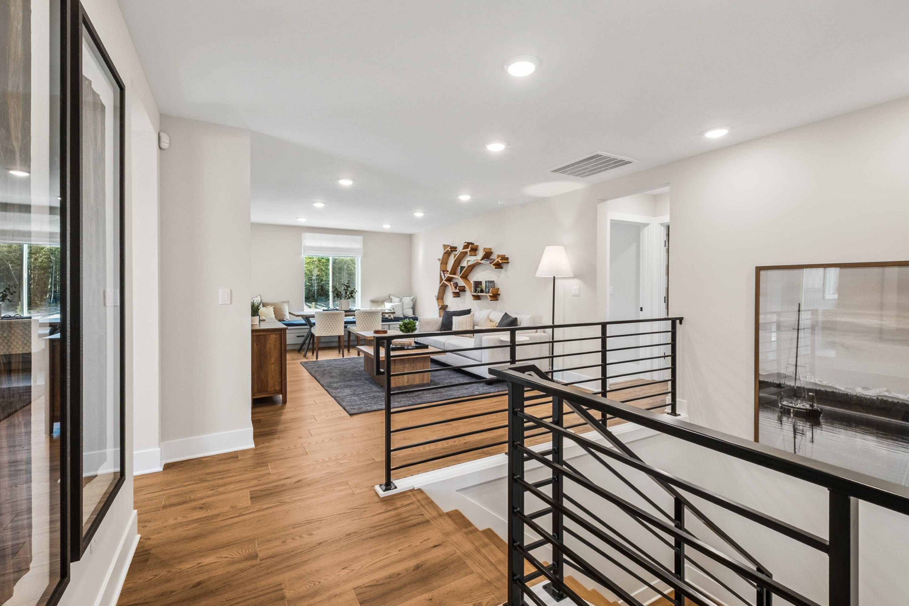 A modern, open-concept living space with a wooden floor, a glass-paneled railing, and a cozy seating area visible in the background.