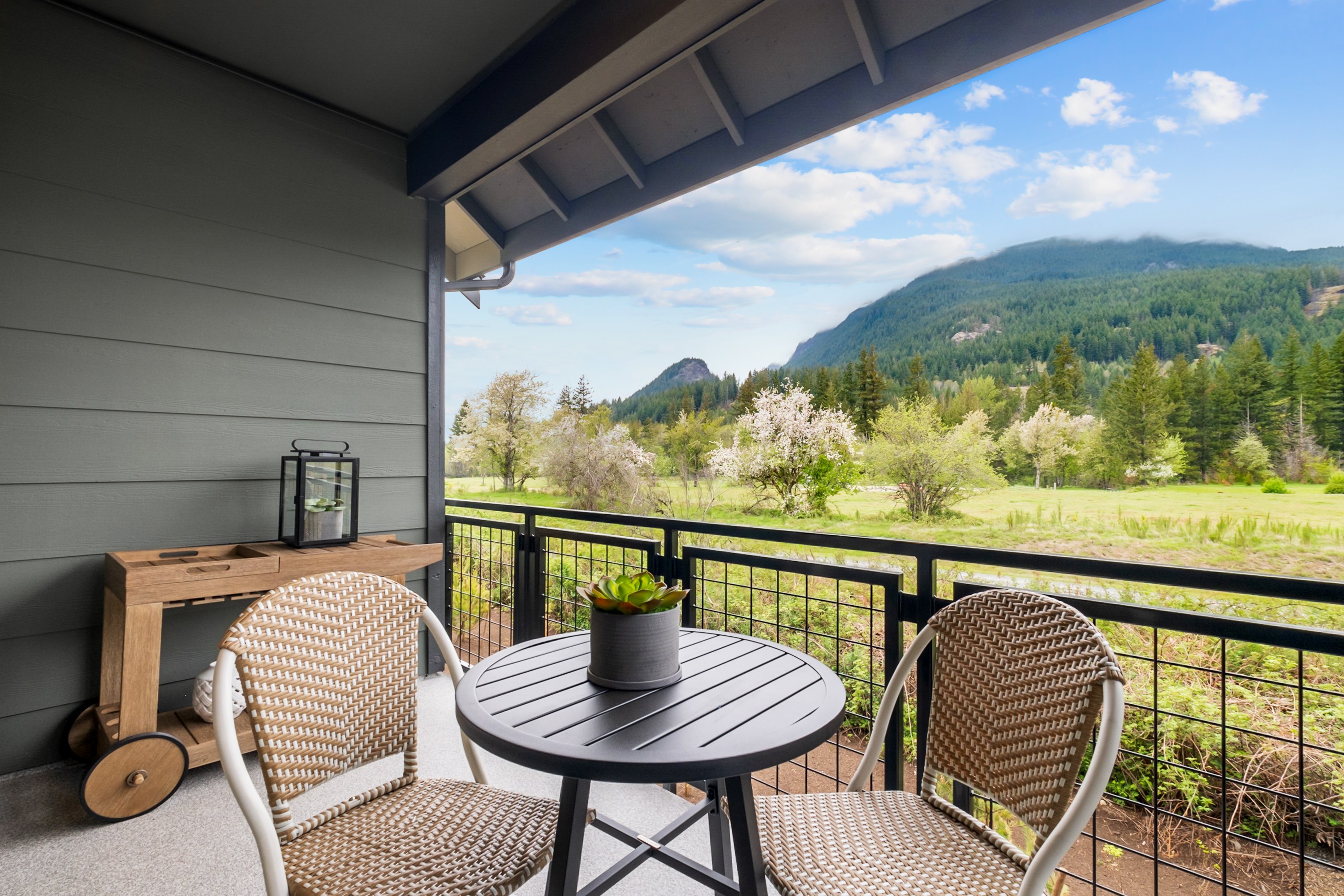 A cozy outdoor seating area on a balcony or patio, with a scenic mountain landscape visible in the background through the open windows.