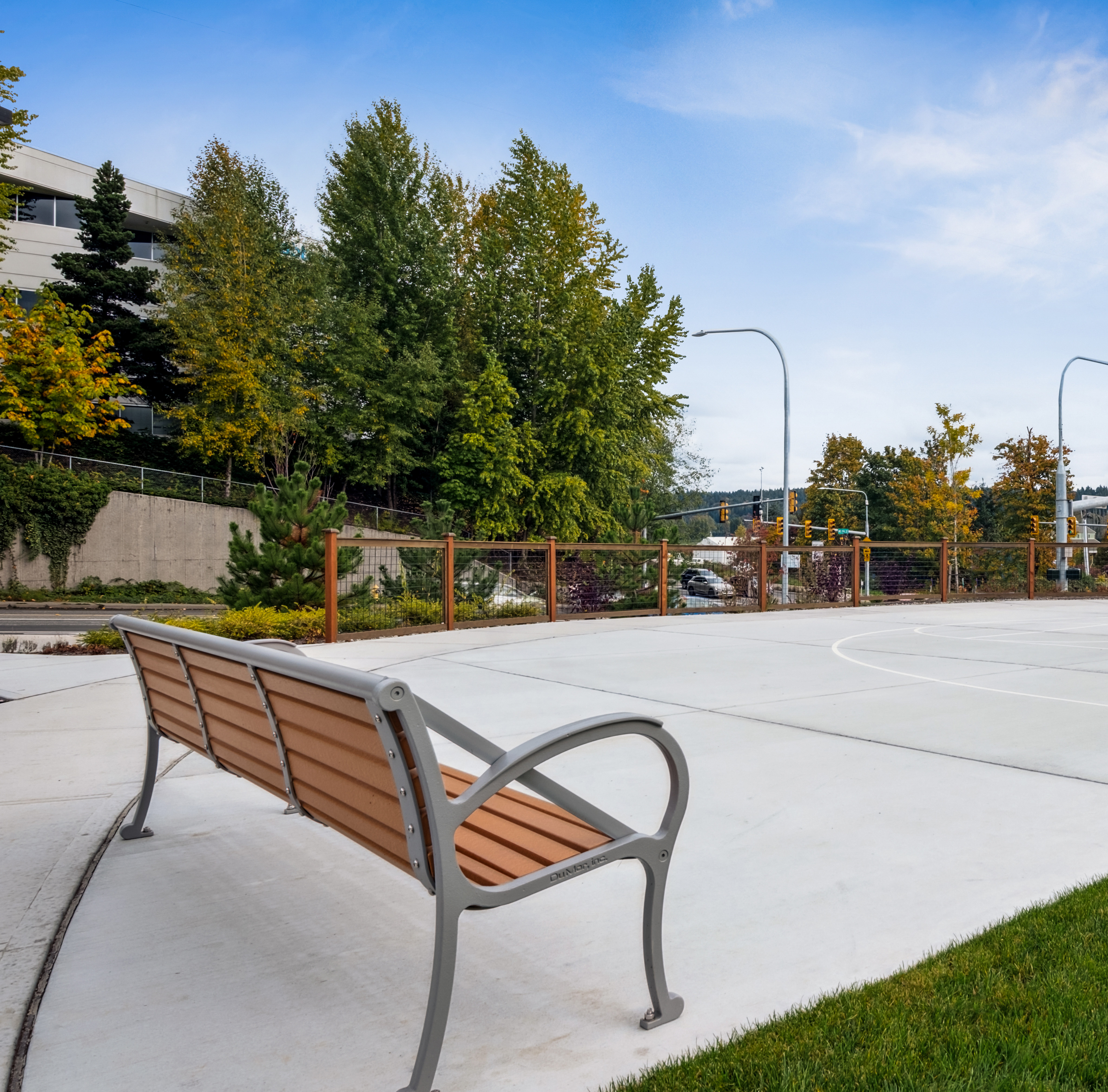 A paved basketball court surrounded by trees and benches, with a clear blue sky overhead.