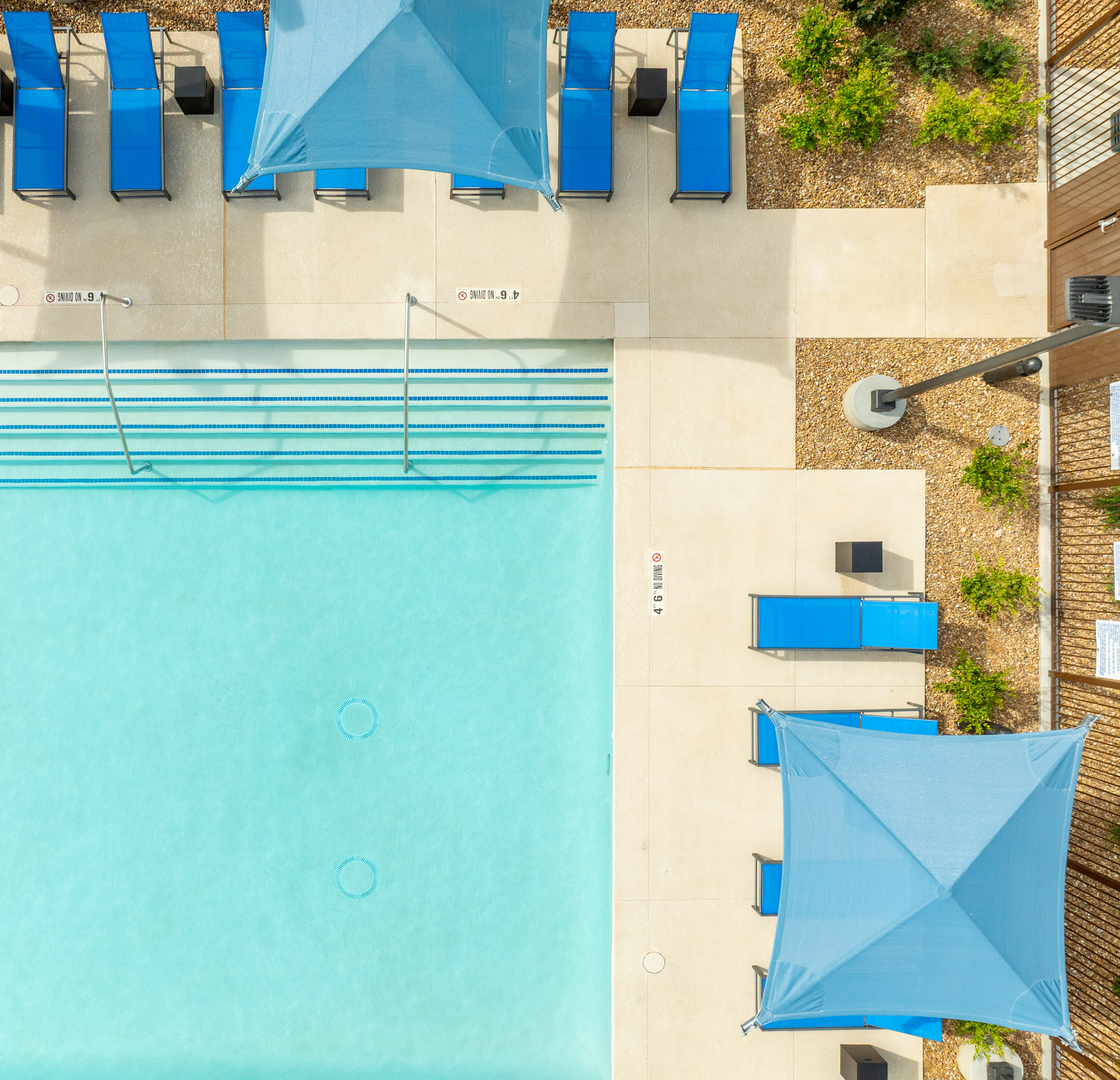 A vibrant, turquoise swimming pool surrounded by blue and white architectural elements, with lush greenery visible in the background.