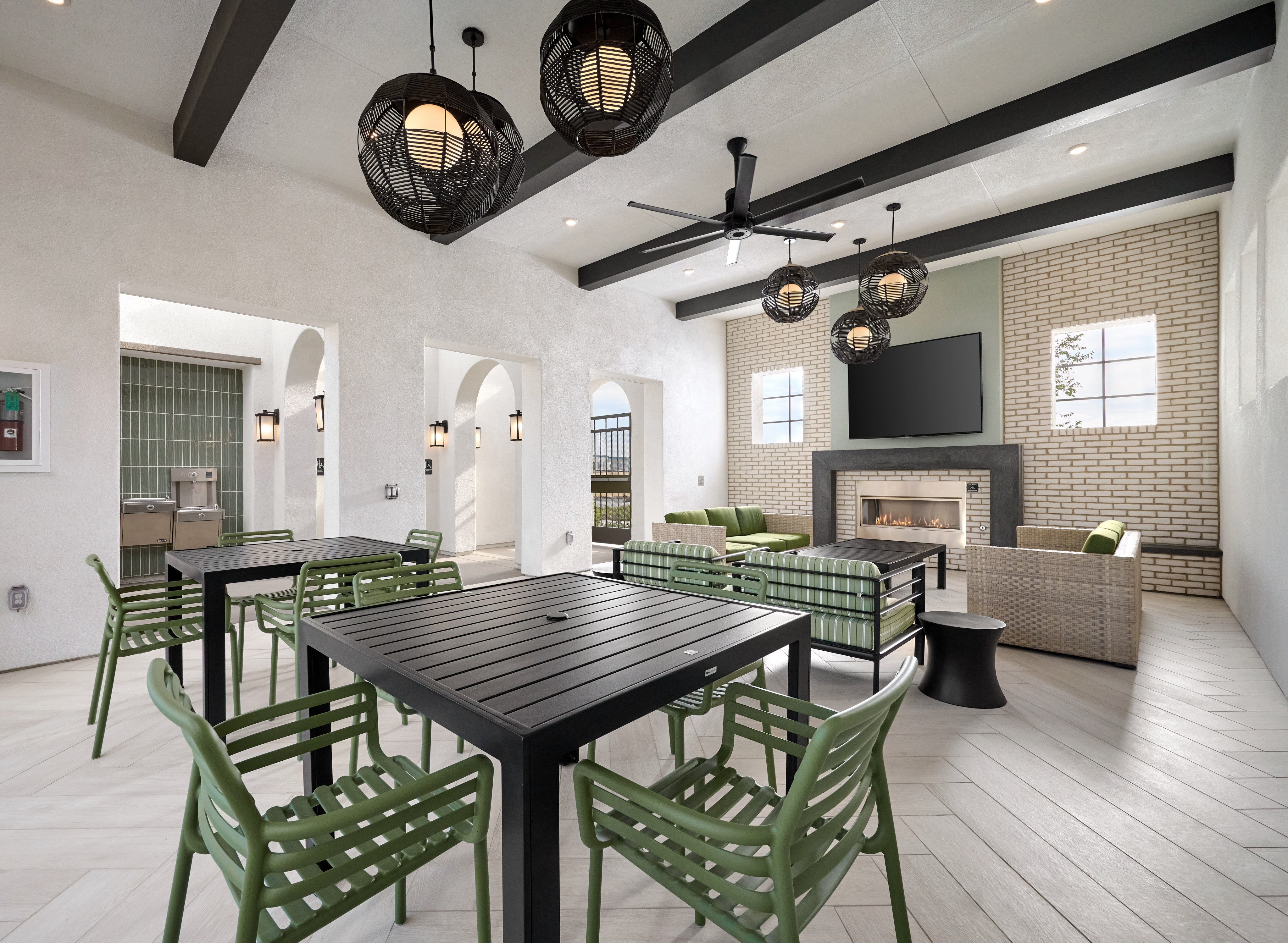 A modern and stylish dining area with a large wooden table surrounded by green metal chairs, complemented by a high ceiling with exposed beams and decorative pendant lights.