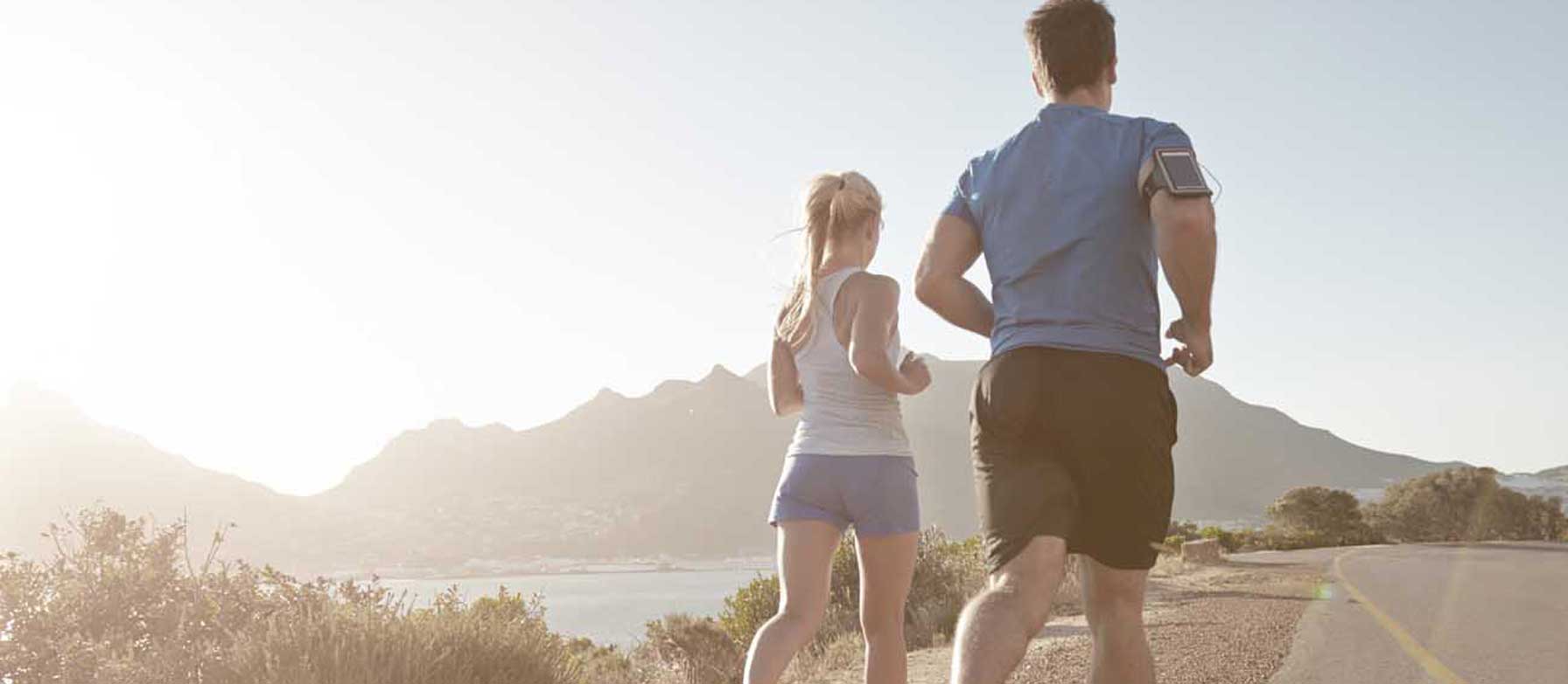 A man and a woman stand together, facing a scenic landscape with mountains and a body of water in the background.