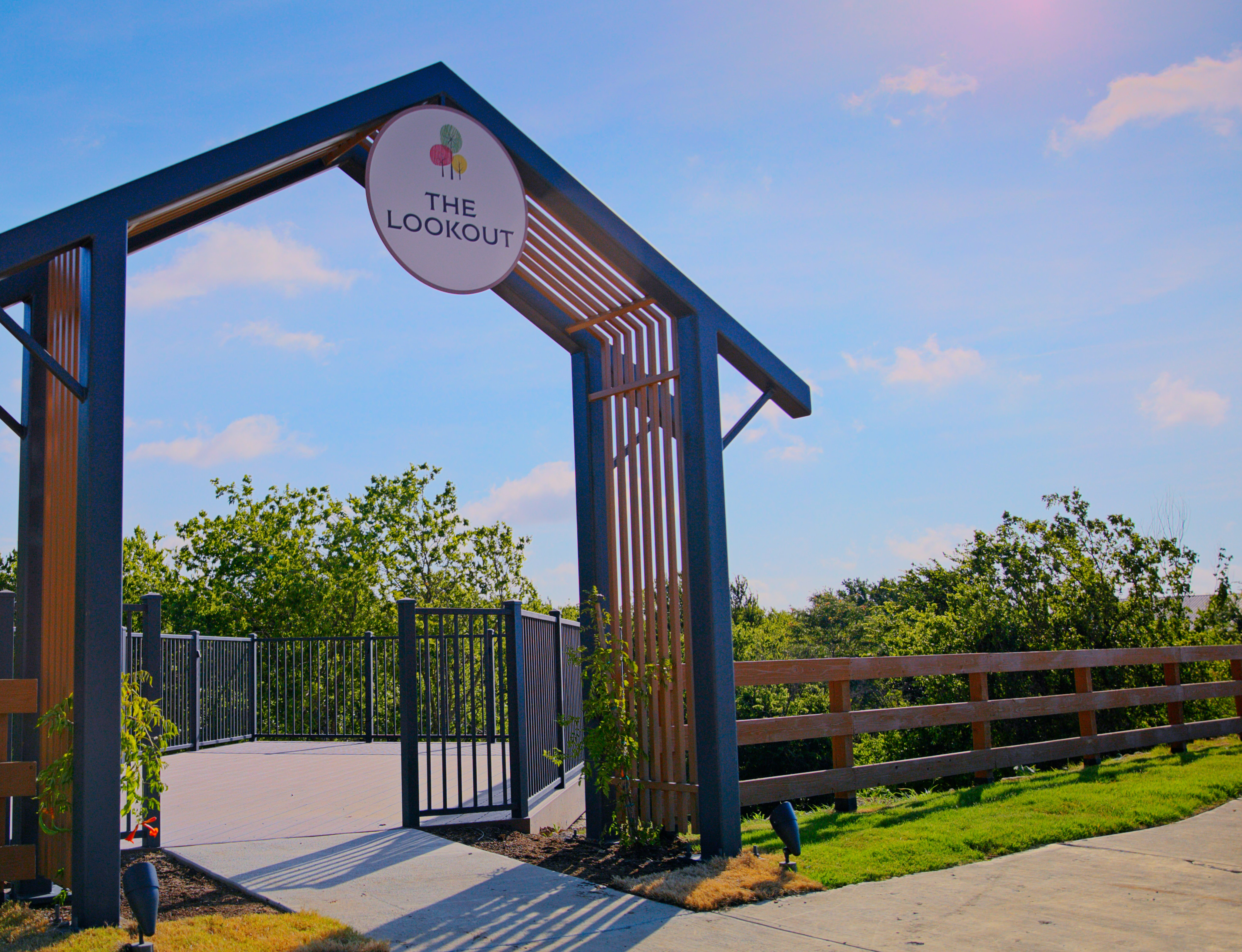 A large metal archway with the text "The Loop" stands in the foreground, surrounded by lush greenery and a paved walkway in the background.