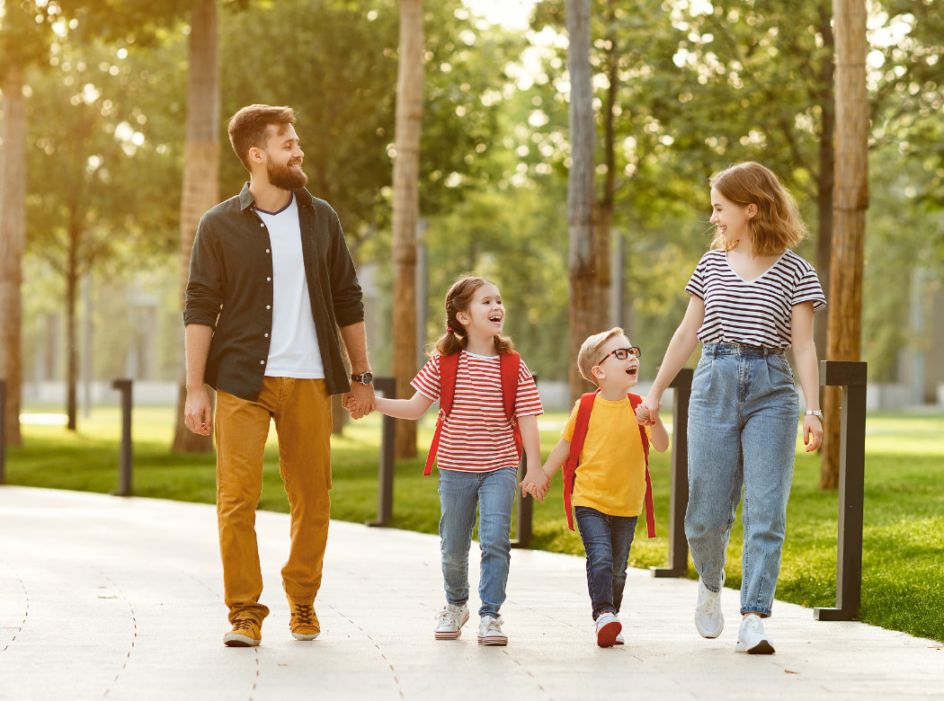 A family of four, consisting of a man, woman, and two children, are walking together on a path surrounded by trees and greenery.