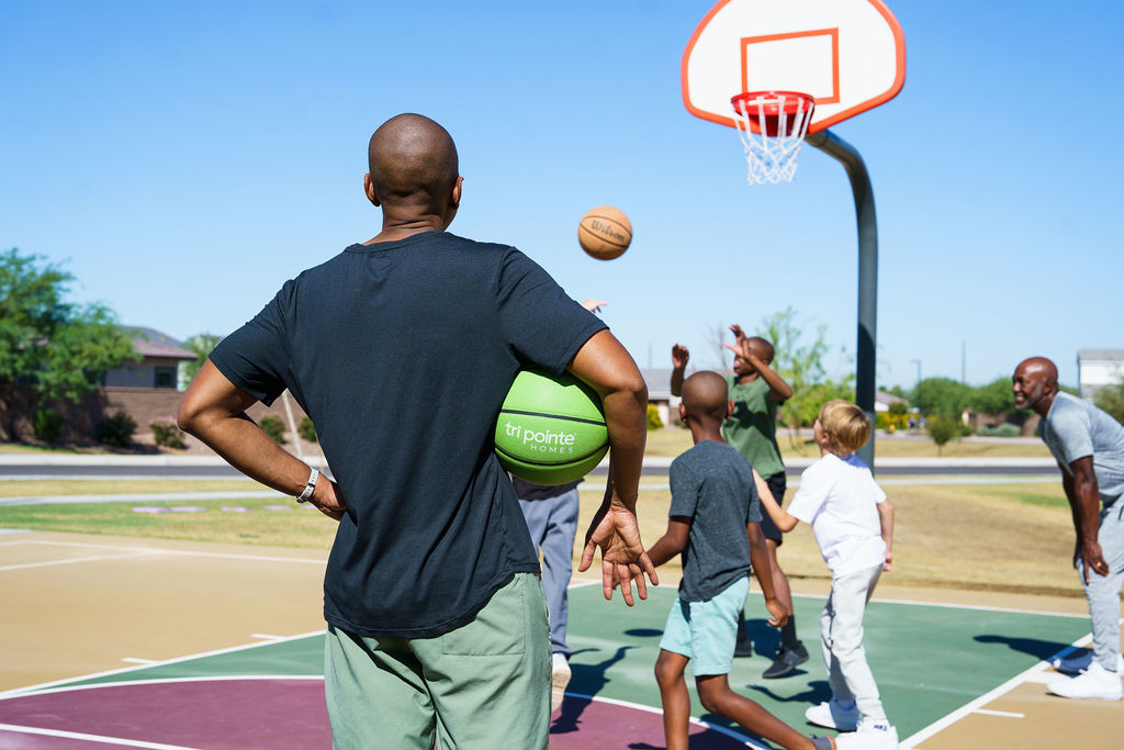 A person in a black shirt is holding a basketball on a basketball court, with other people visible in the background.