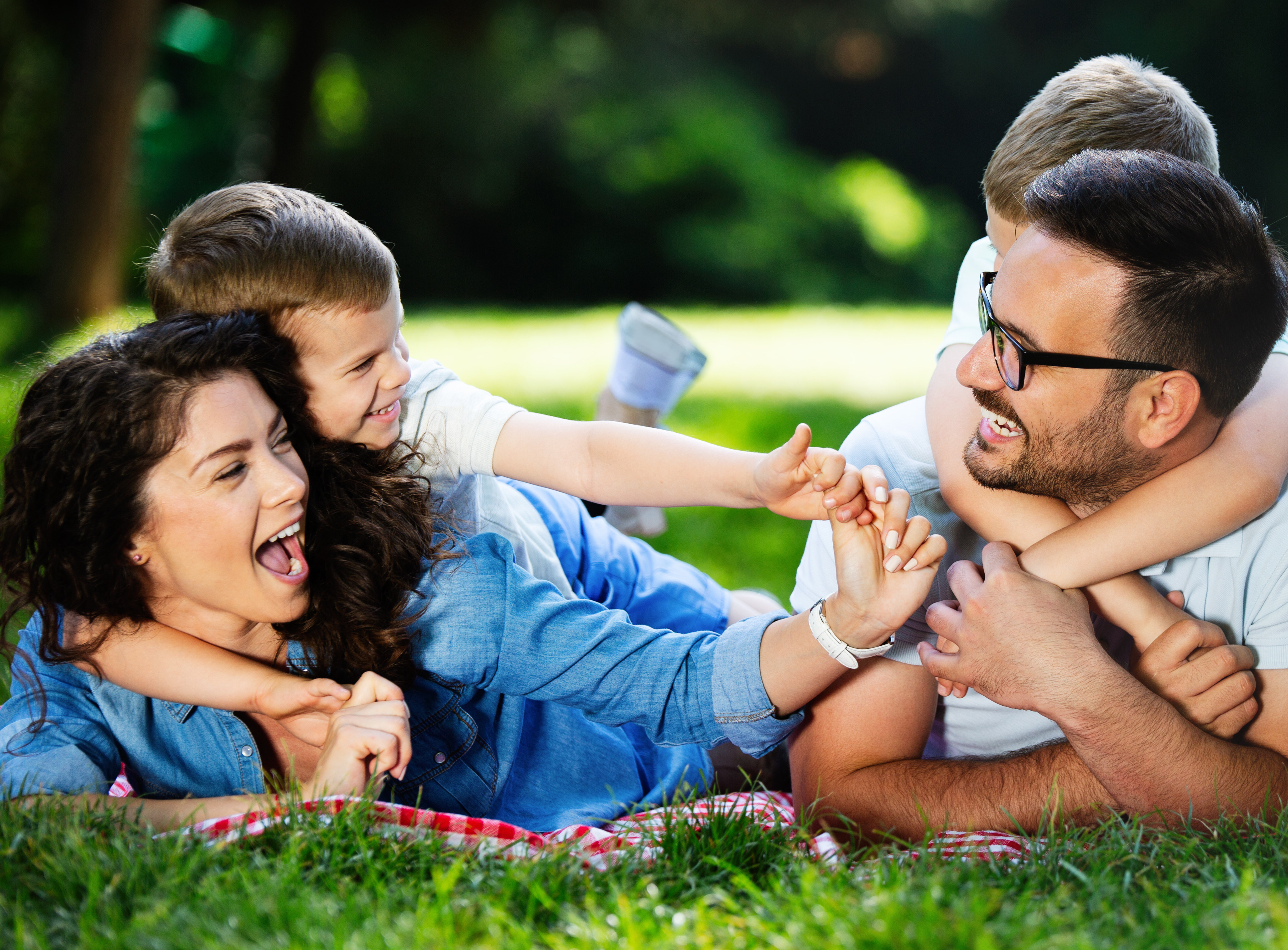 A happy family enjoying a picnic in a lush, green outdoor setting, with the adults playfully interacting with the child.