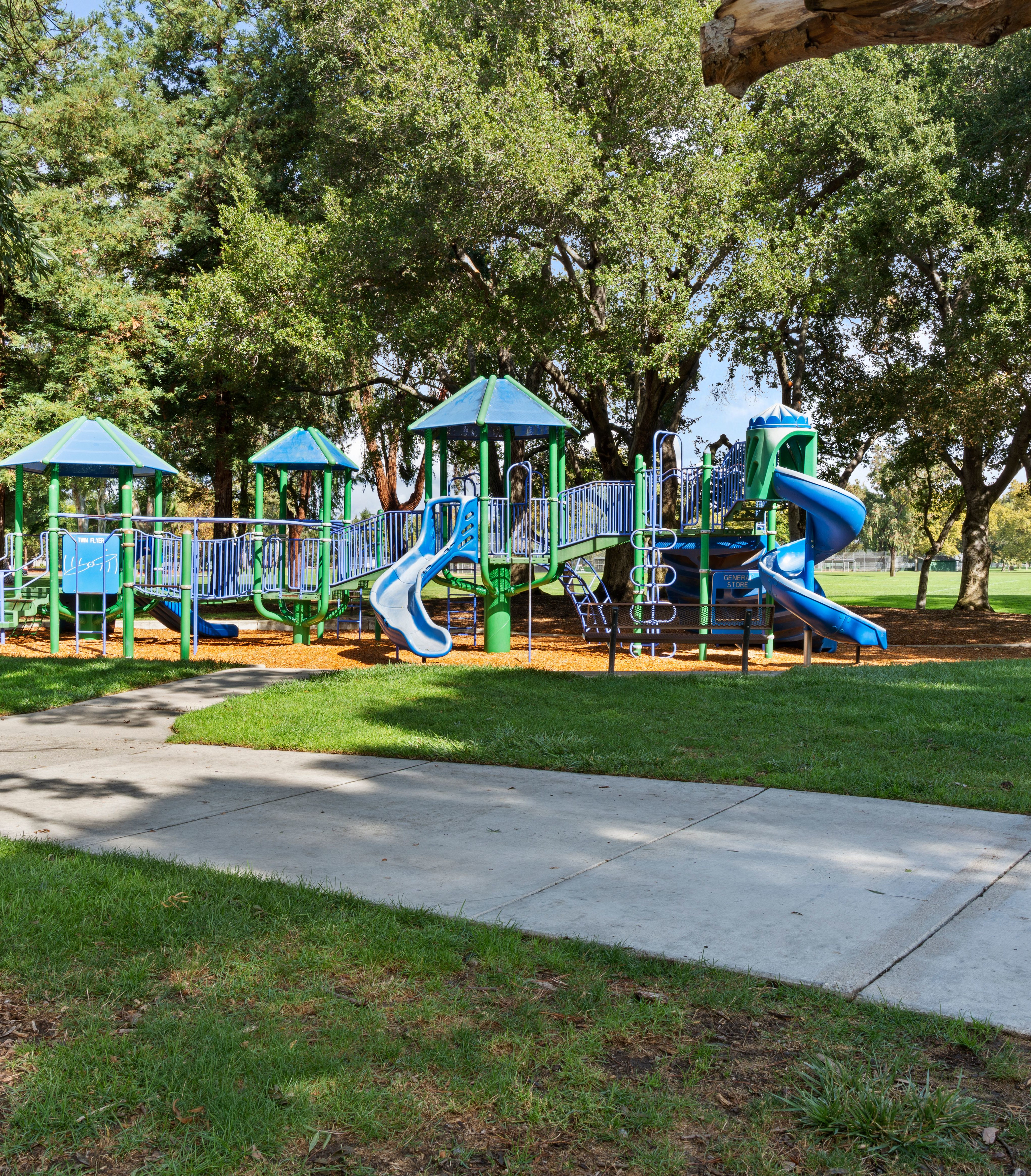 A colorful playground with various play structures, surrounded by lush greenery and trees, sits in a well-maintained park setting.