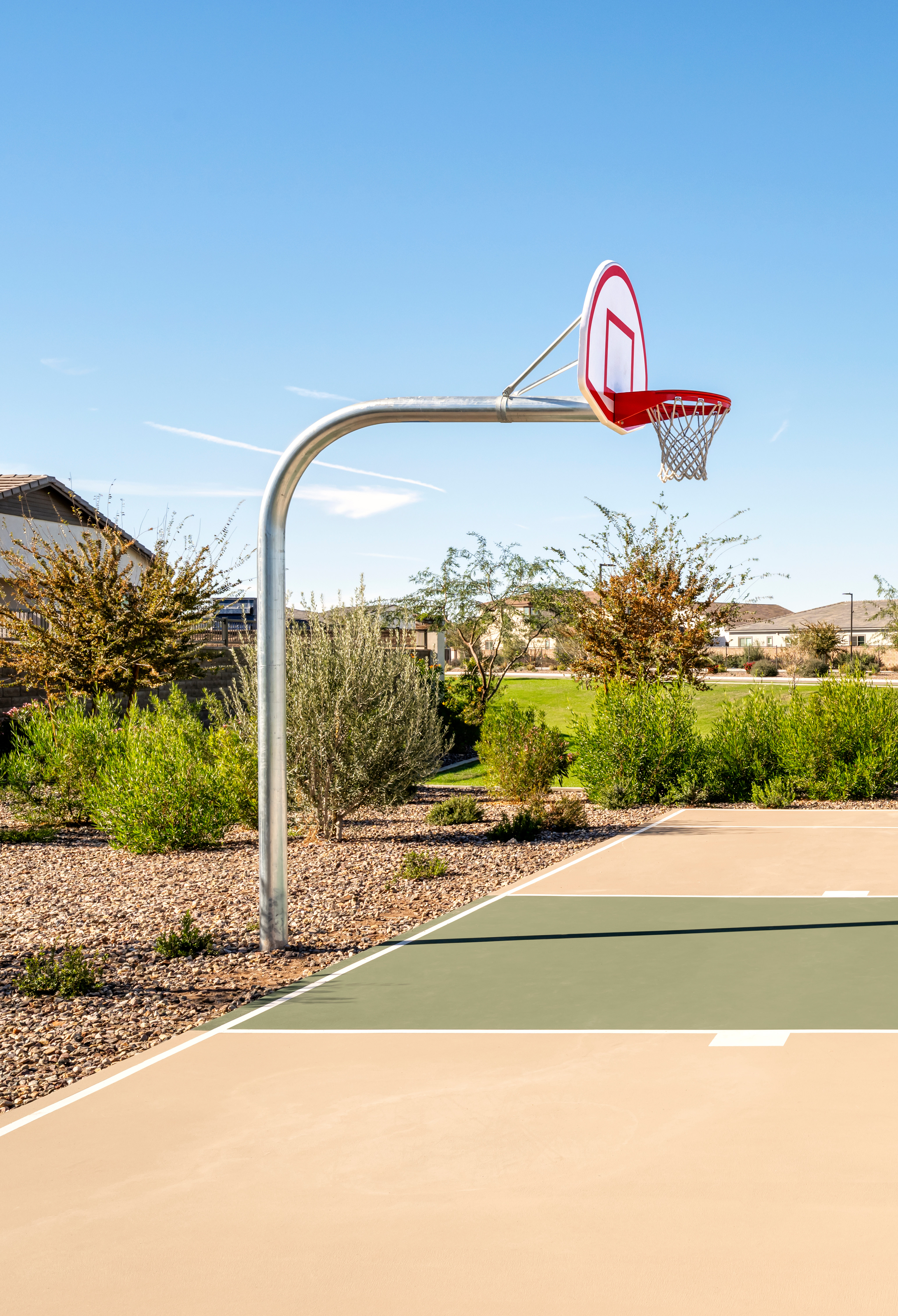 A basketball court with a hoop and backboard stands in the foreground, surrounded by a well-maintained landscaped area with houses visible in the background.