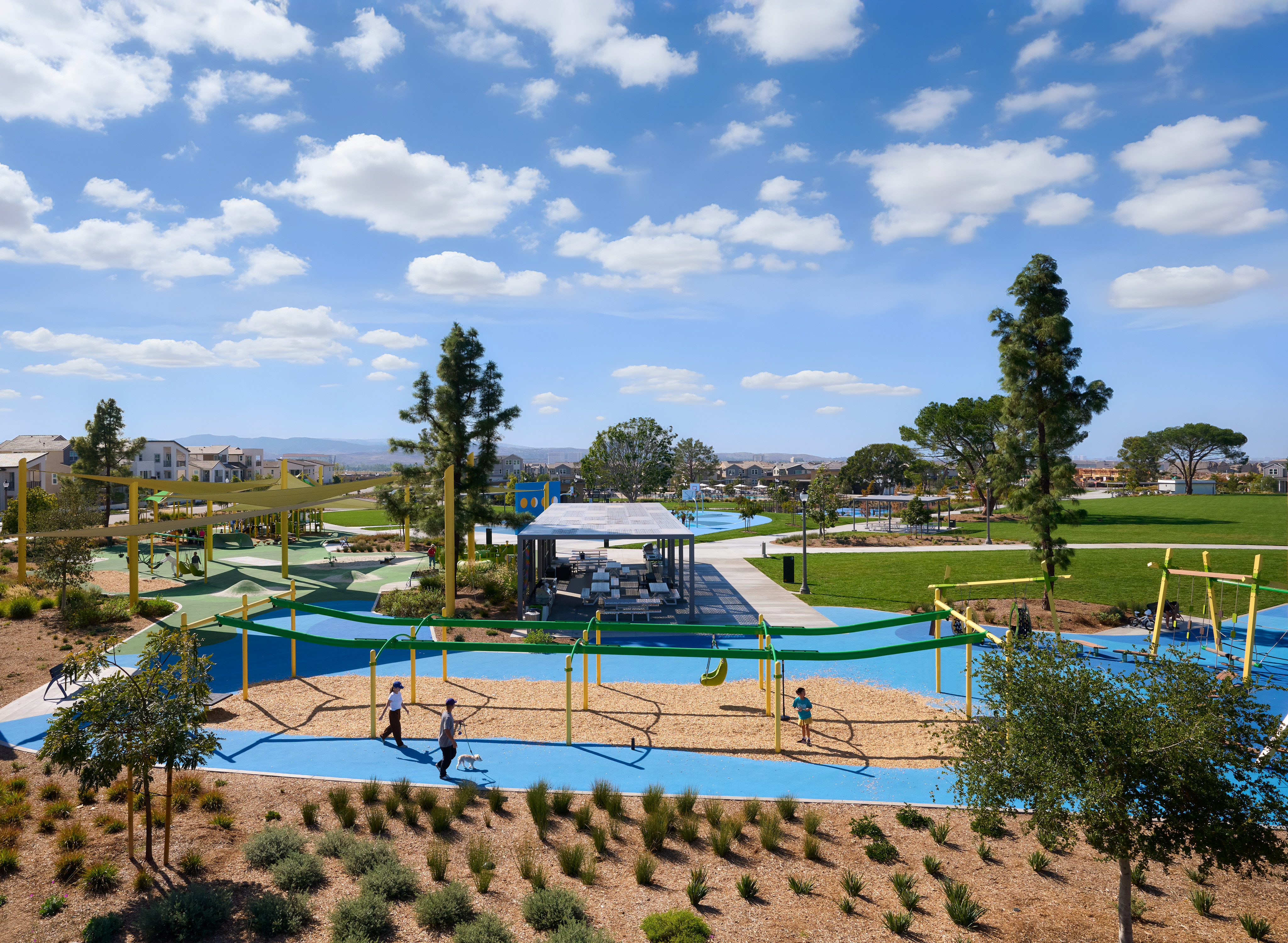 A vibrant outdoor recreational area with a colorful water park, surrounded by lush greenery and a clear blue sky dotted with fluffy white clouds.