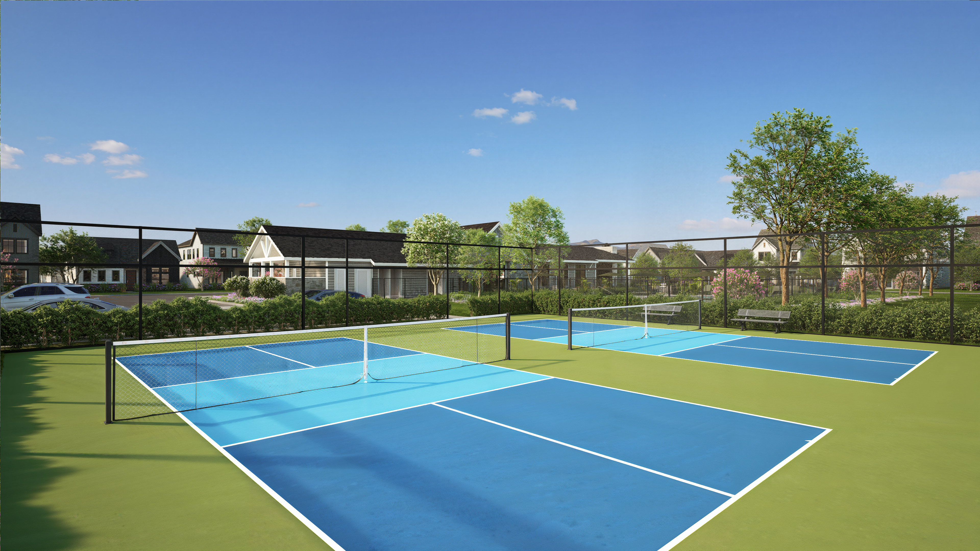 Two bright blue pickleball courts with white lines are in the foreground, while a residential neighborhood with houses and trees is in the background under a clear blue sky.