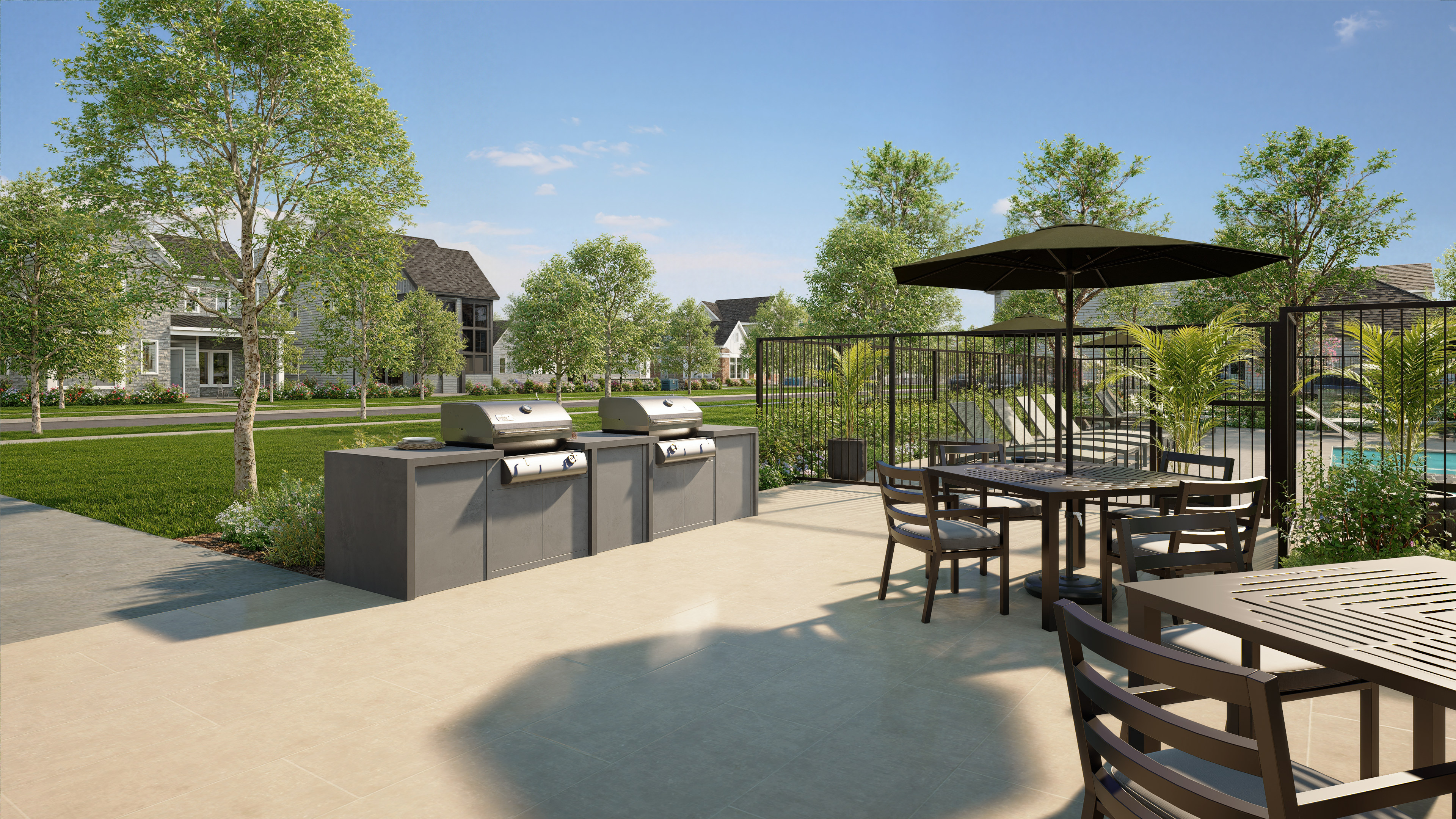 Two stainless steel grills sit on a concrete patio in the foreground, with a swimming pool and apartment buildings visible in the background.