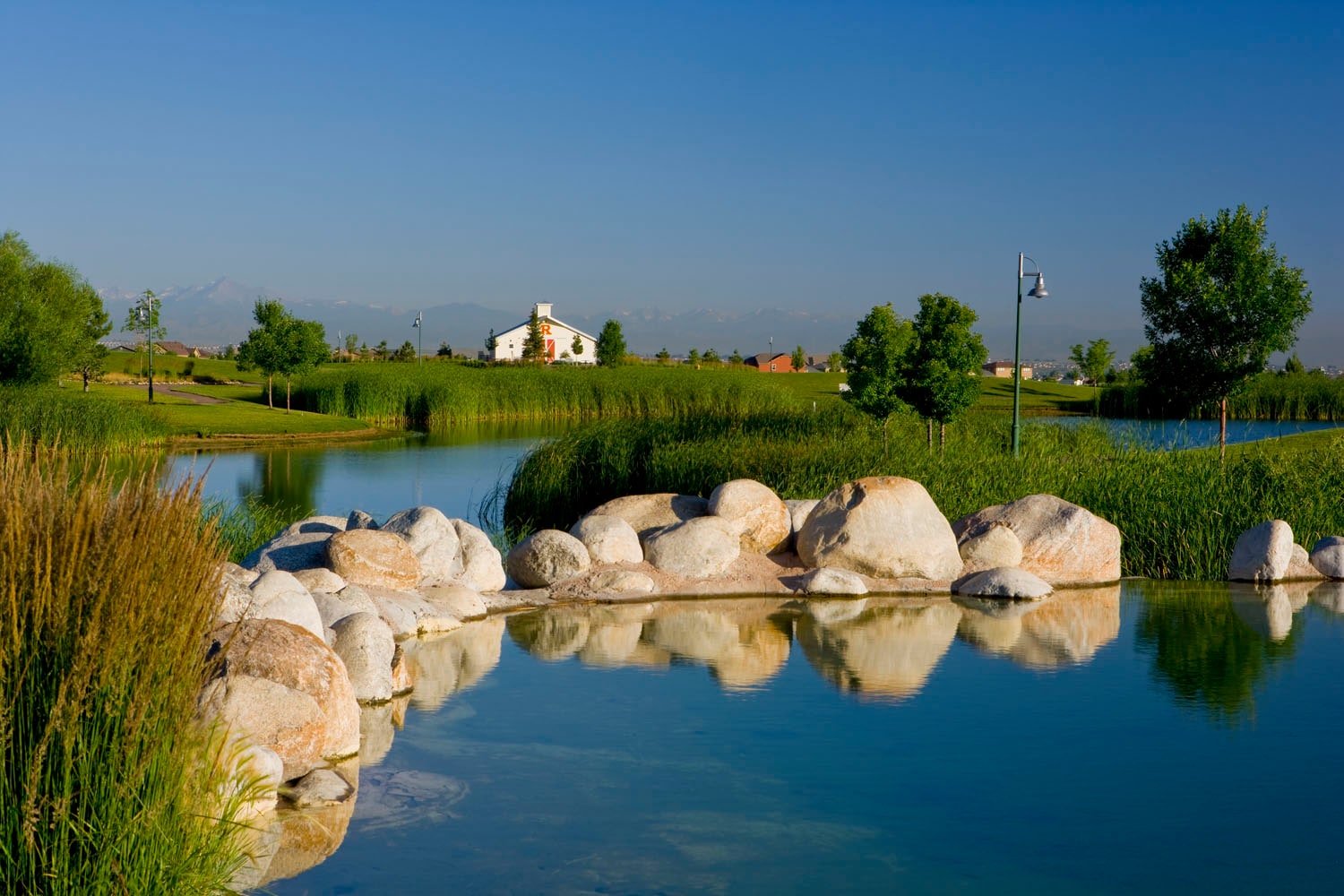 A serene pond surrounded by large boulders, with a lush green landscape and a clear blue sky in the background.