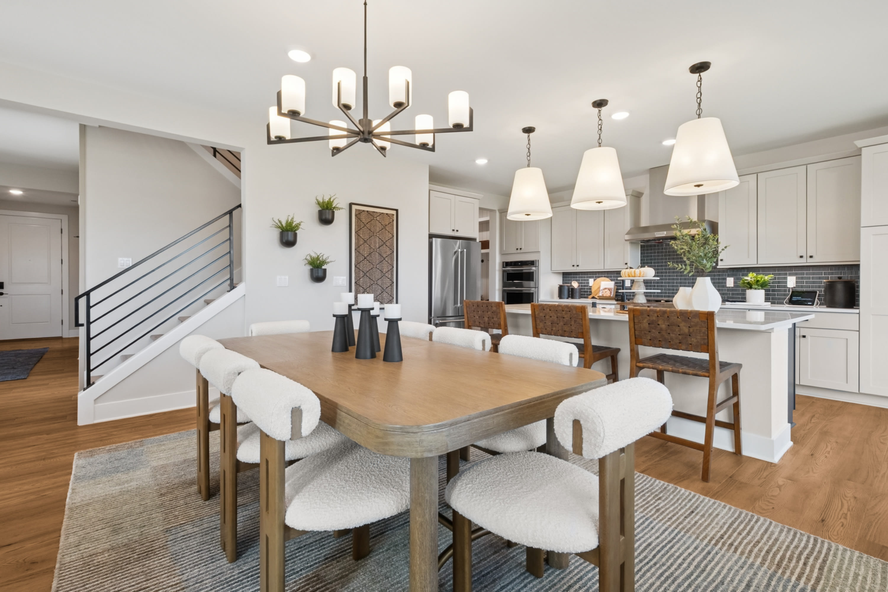 A modern and spacious kitchen and dining area with a wooden dining table, white chairs, and various pendant lights hanging from the ceiling.