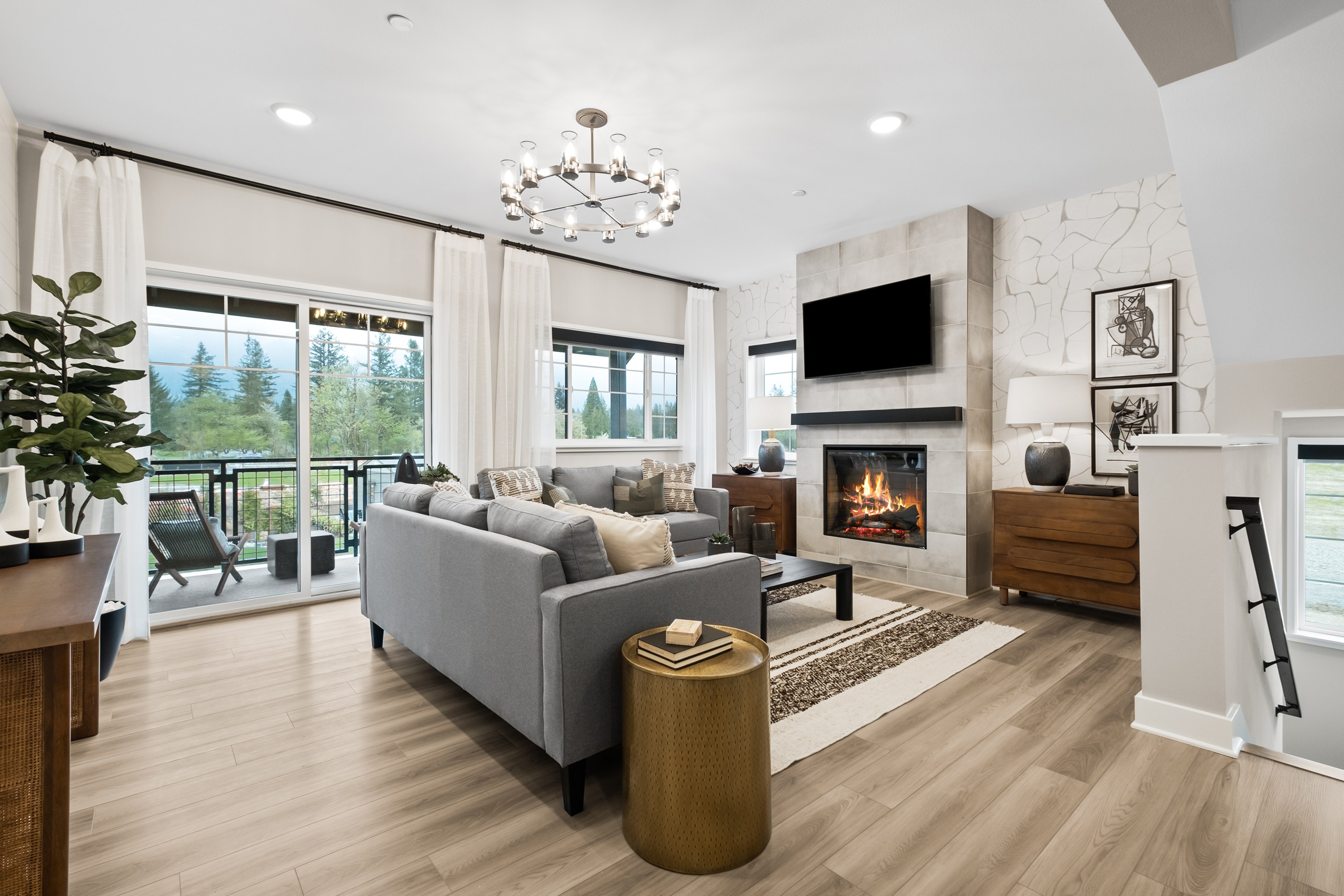 A cozy and modern living room with a fireplace, gray sofas, and large windows overlooking a scenic outdoor view.