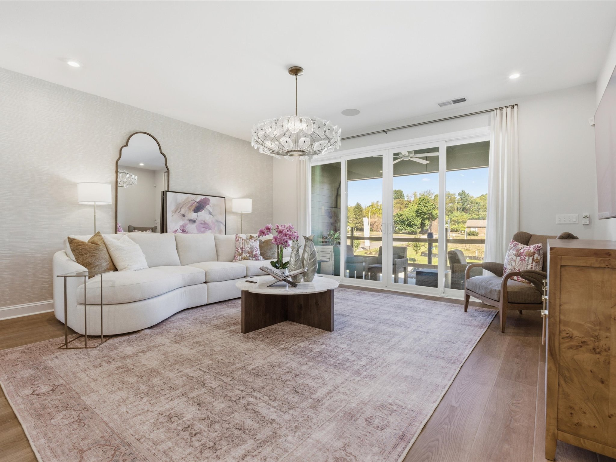 A spacious and elegantly furnished living room with a curved sofa, a wooden coffee table, and a large window overlooking a scenic outdoor view.