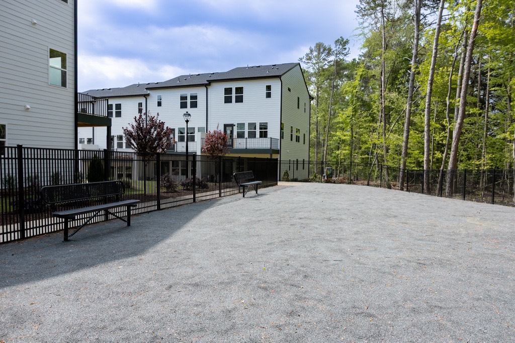 A paved walkway leads to a multi-story residential building surrounded by trees in a wooded area.
