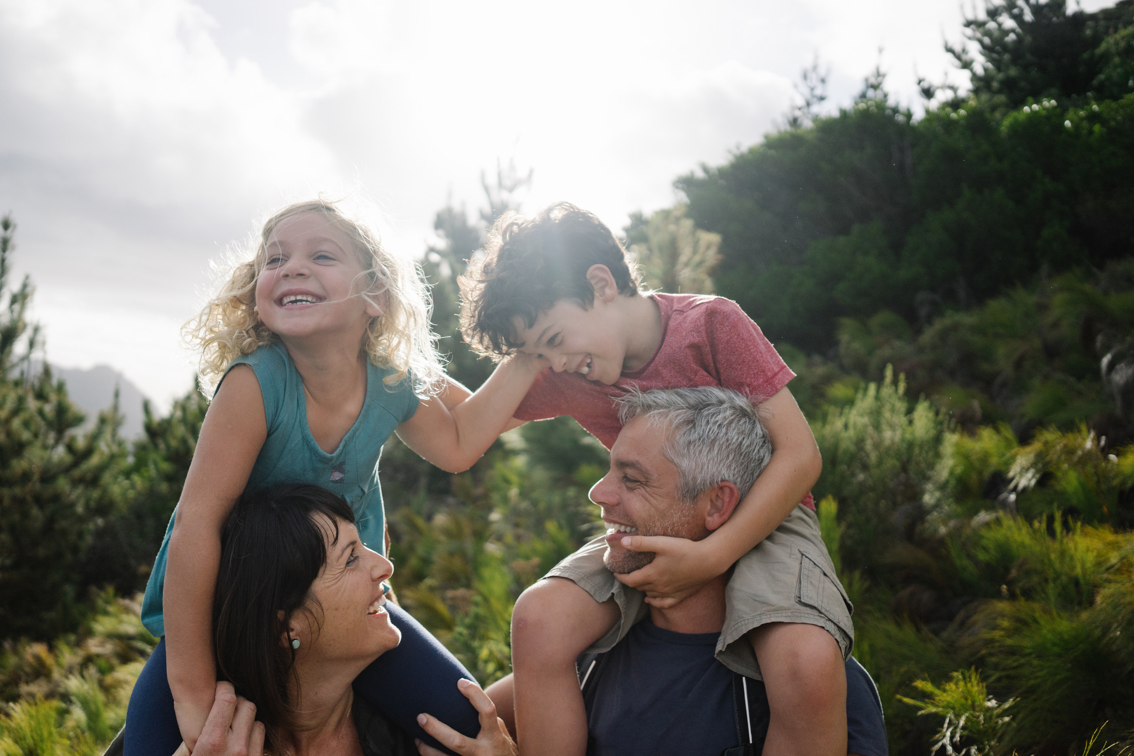 A family of four - two adults and two children - enjoying a moment together outdoors in a lush, forested setting.