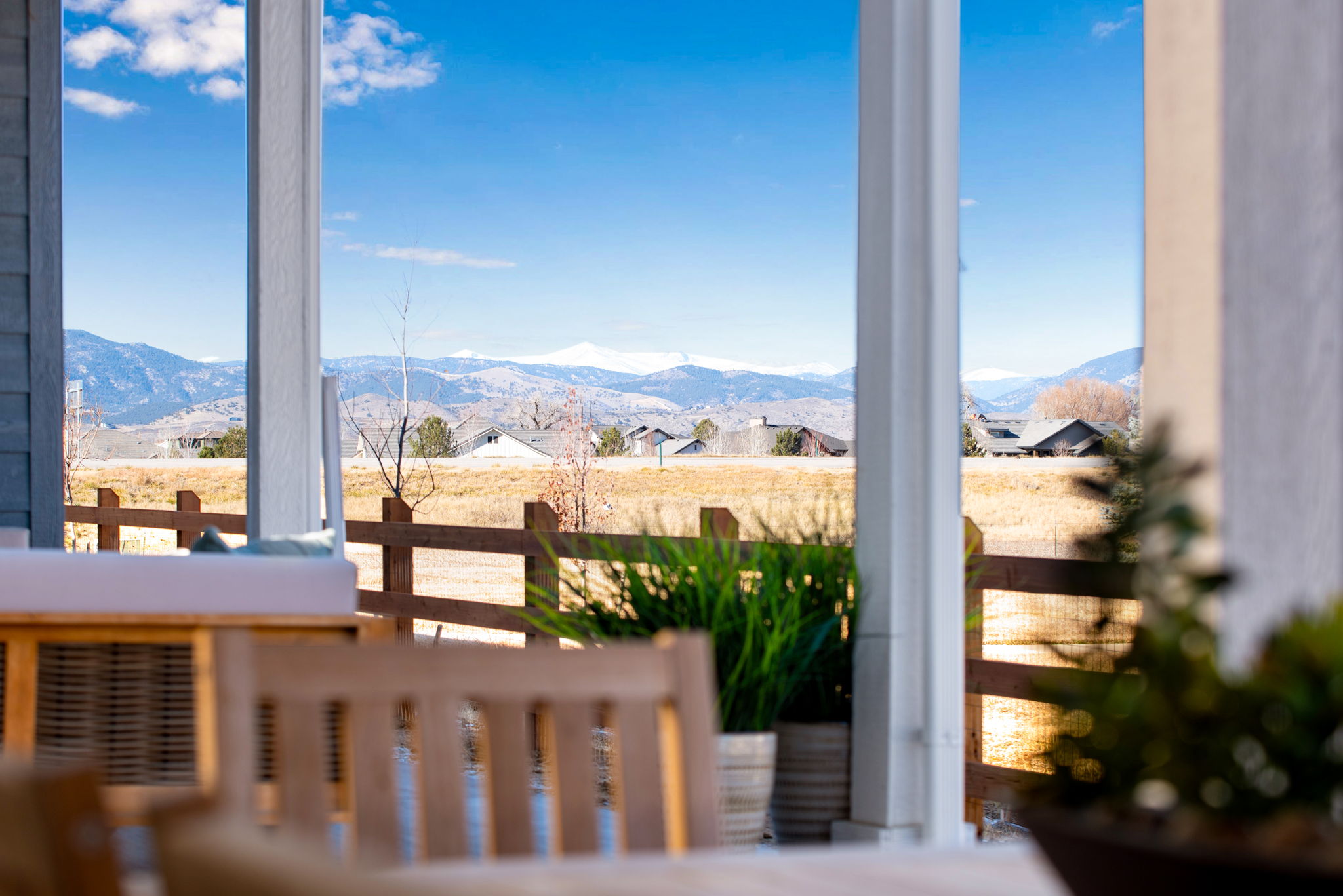 A cozy wooden porch overlooking a picturesque rural landscape with mountains in the distance under a bright blue sky with fluffy clouds.