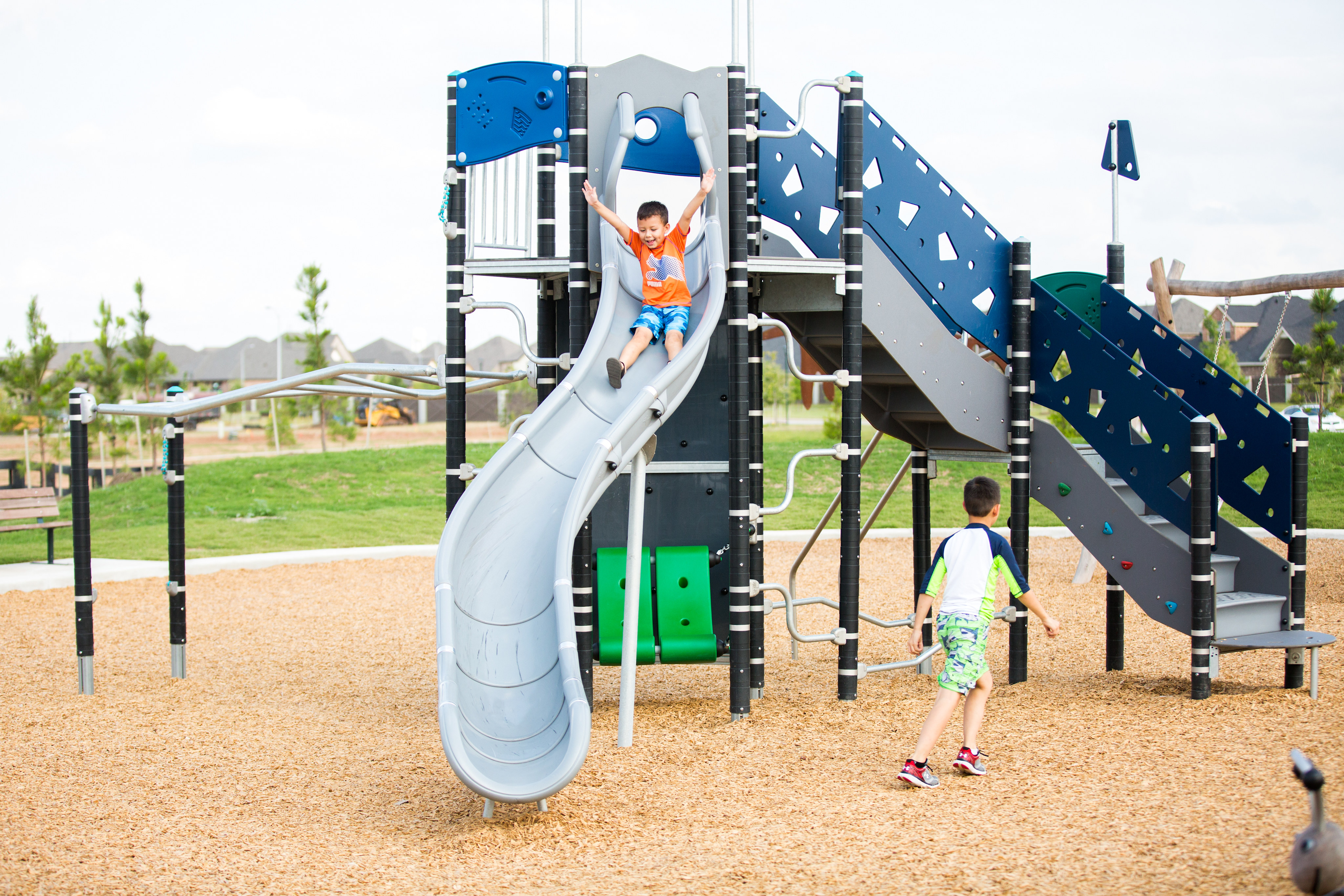 A colorful and modern playground with various slides, climbing structures, and a child playing on the equipment in the foreground.