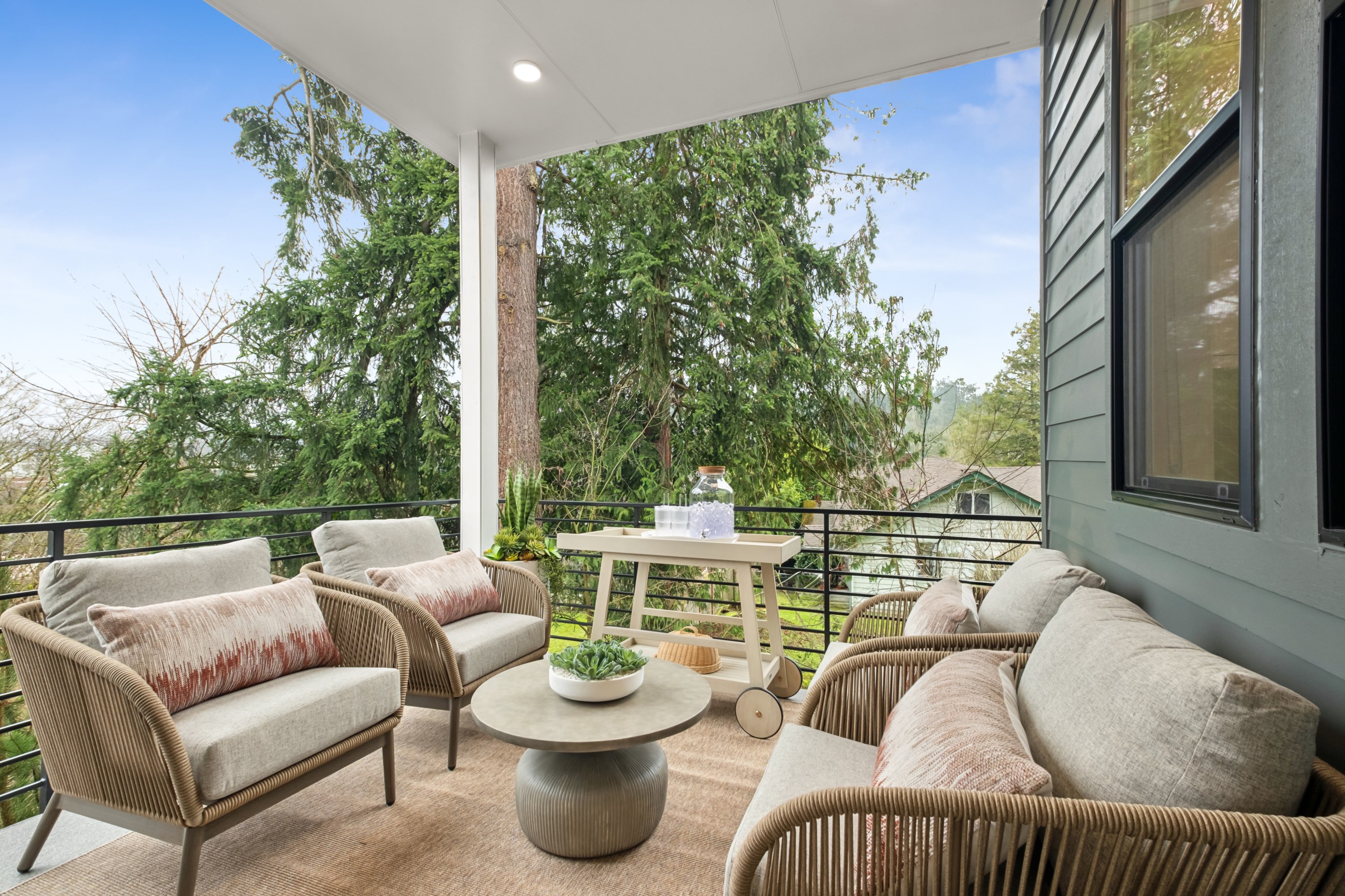 A cozy outdoor seating area with comfortable wicker furniture, surrounded by lush greenery and a clear blue sky.