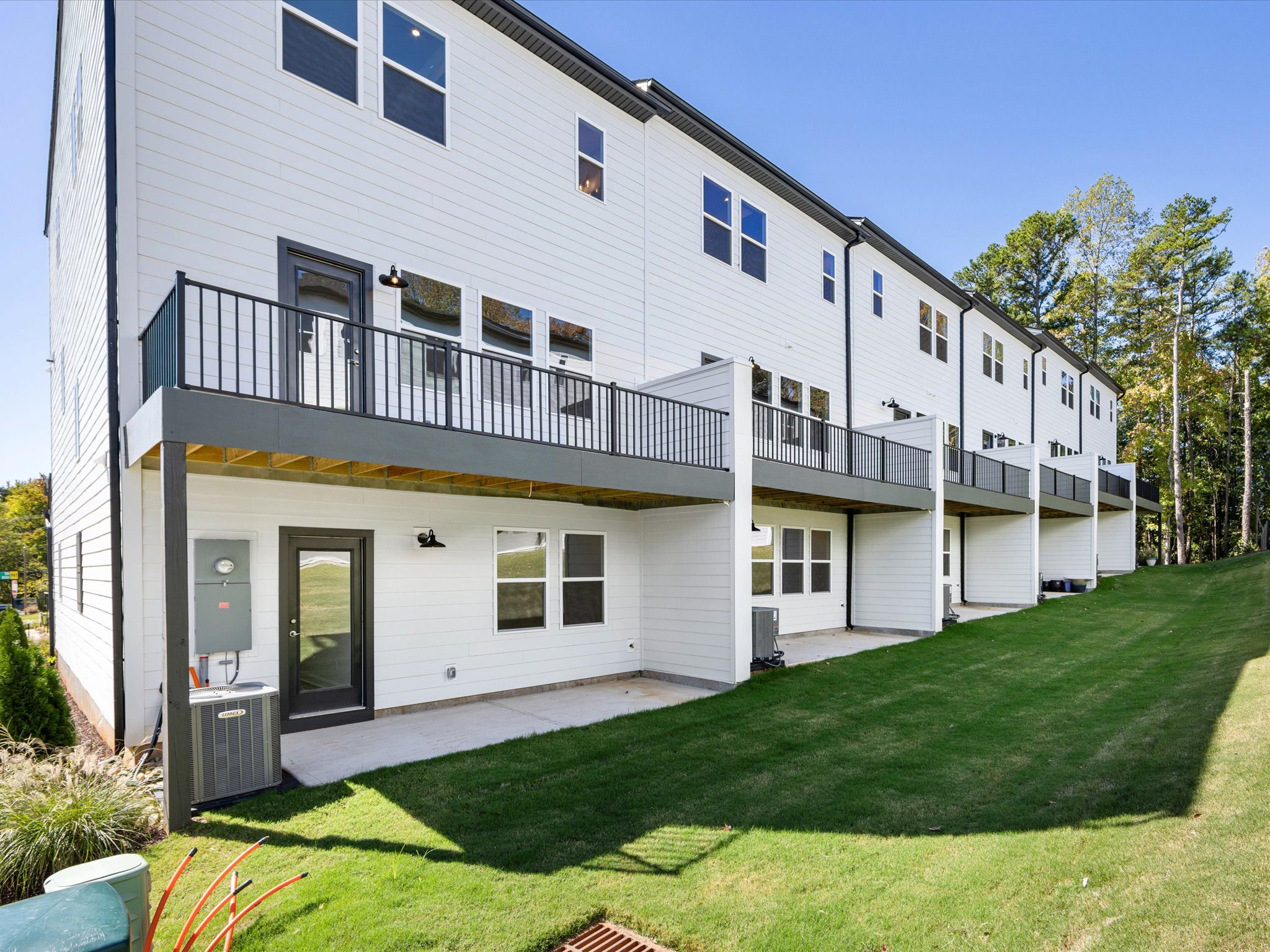 A multi-story residential building with a grassy lawn in the foreground and trees in the background, featuring balconies and a modern architectural design.