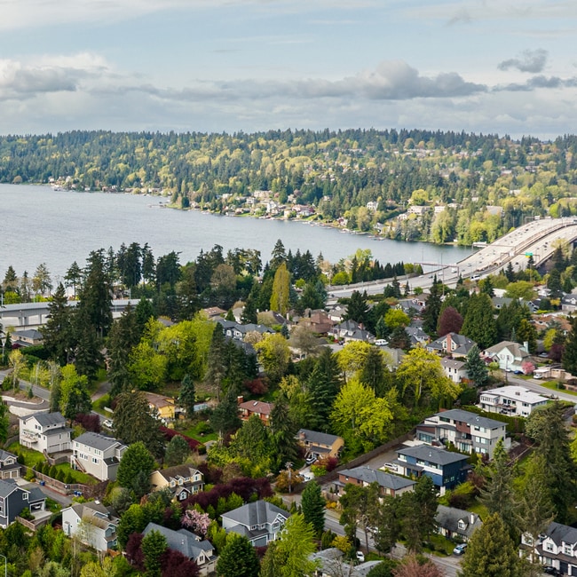 A scenic view of a residential neighborhood nestled among lush greenery, with a lake and mountains visible in the background.