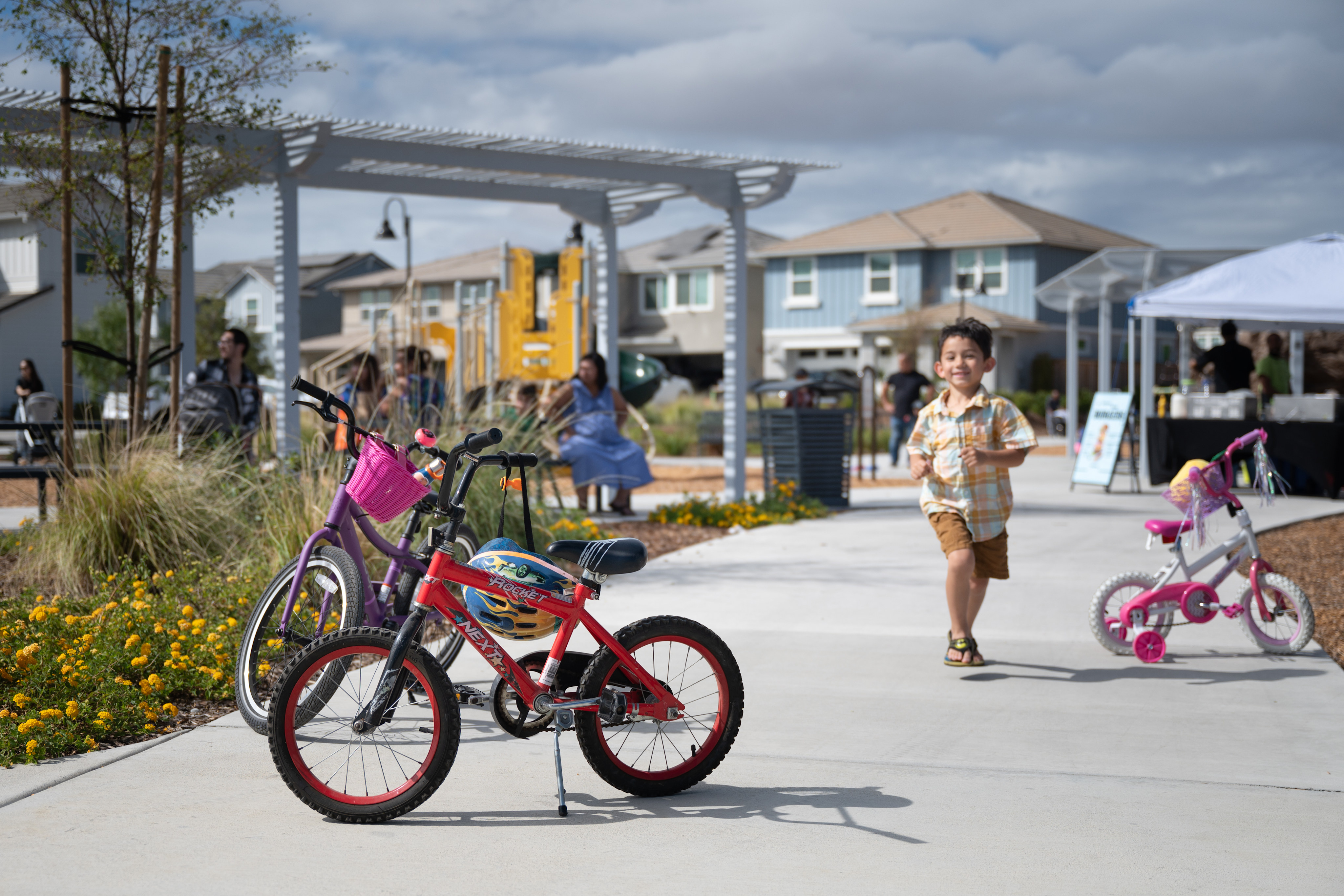 A vibrant outdoor shopping area with colorful bicycles and children playing in the foreground, surrounded by various shops and buildings in the background.