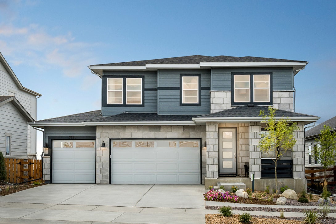 A two-story residential house with a gray exterior, a tiled roof, and a well-landscaped front yard featuring flowers and rocks.