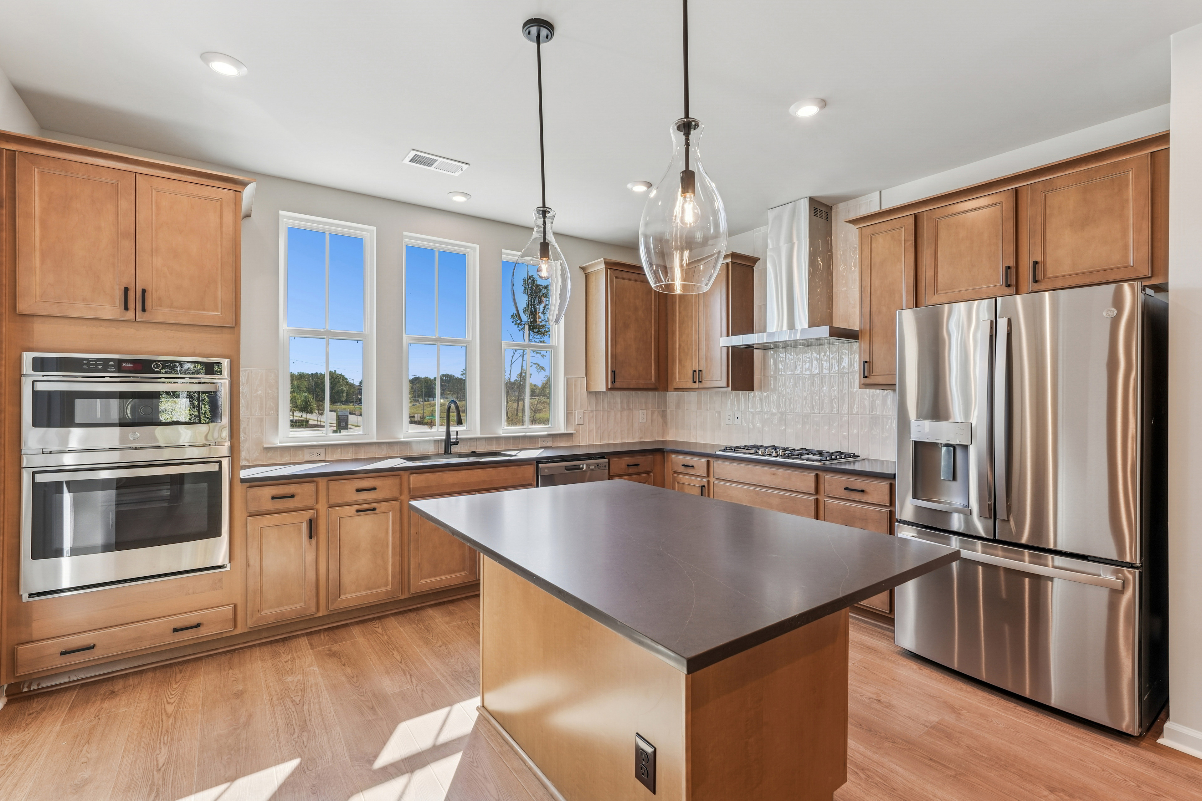 A modern, well-equipped kitchen with wooden cabinets, stainless steel appliances, and a central island with a dark countertop.
