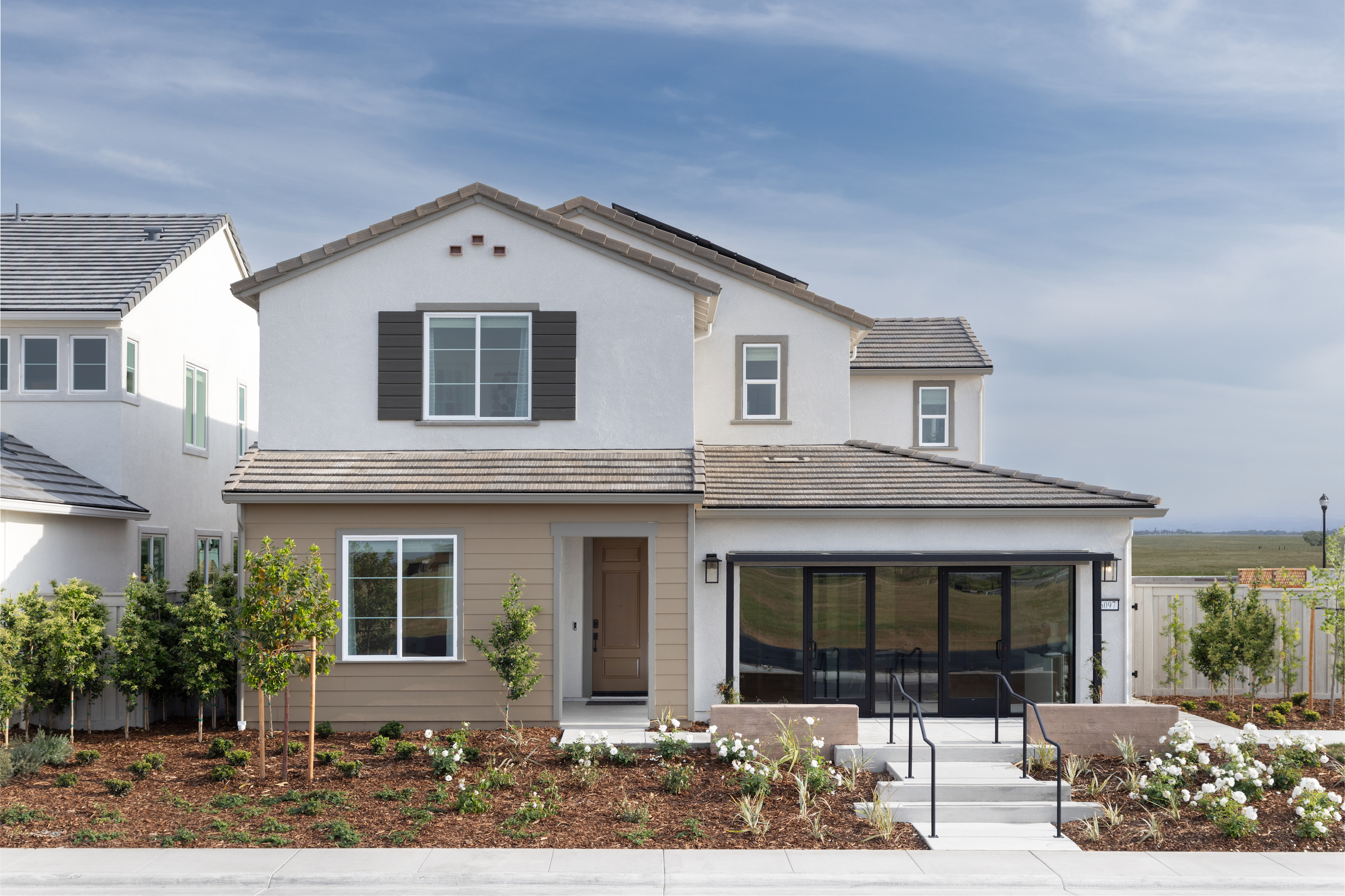 A two-story residential house with a porch, surrounded by a well-maintained garden and a clear blue sky in the background.