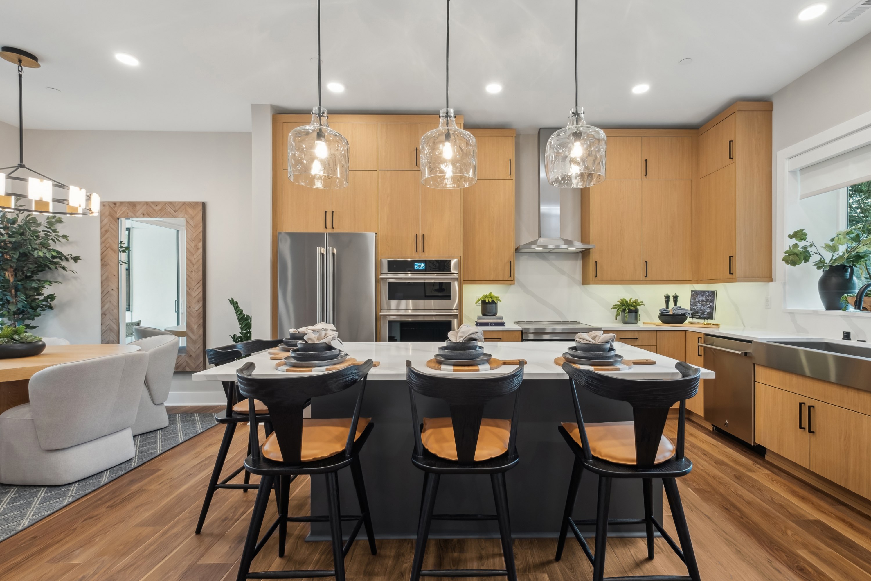 A modern and spacious kitchen with wooden cabinets, stainless steel appliances, and a large island with bar stools, illuminated by pendant lights.