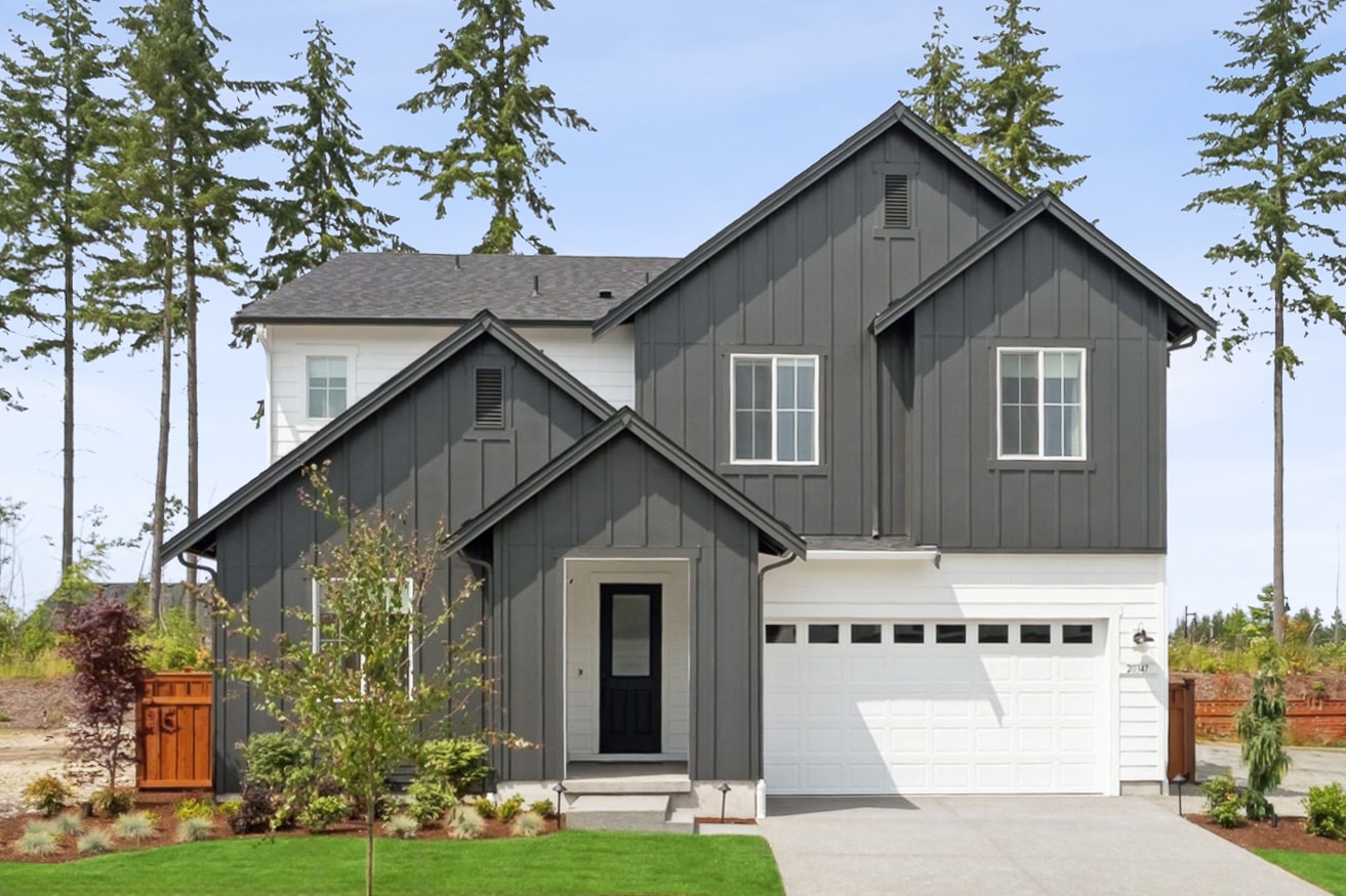 A two-story house with a gray exterior, surrounded by tall pine trees and a well-manicured lawn, stands in the foreground of the image.