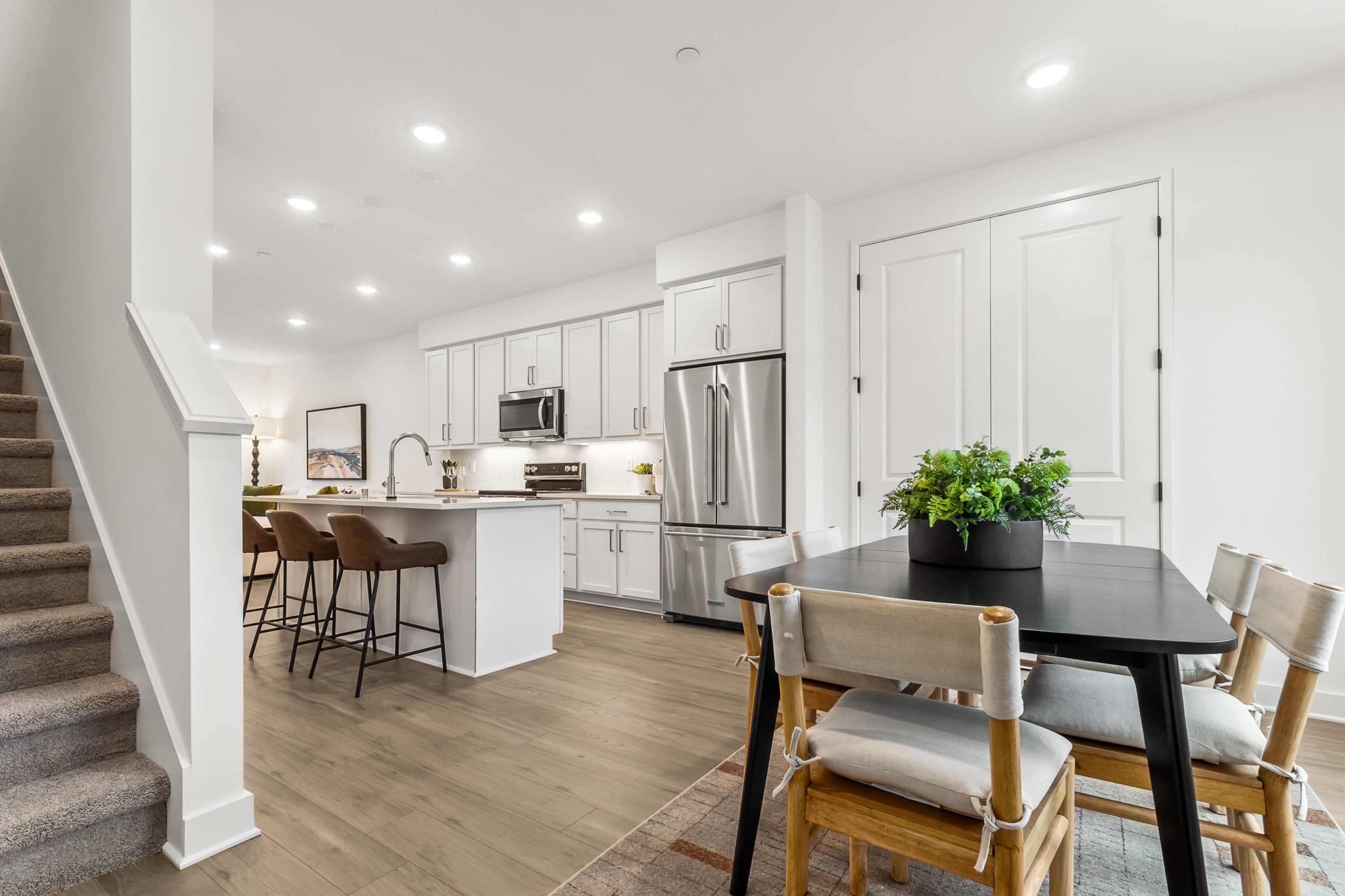 A modern, open-concept kitchen and dining area with white cabinets, stainless steel appliances, and a wooden dining table with chairs.